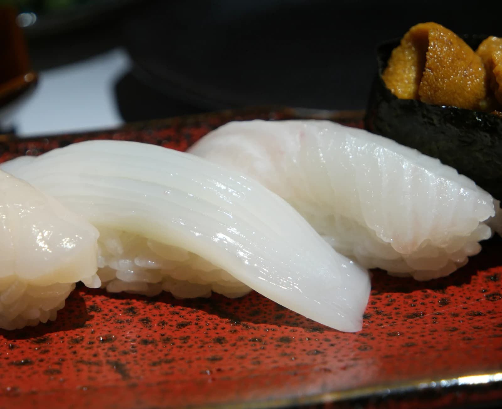 Sushi de calmar tranché finement sans entailles préservant la fibre, blanc translucide sur assiette rouge