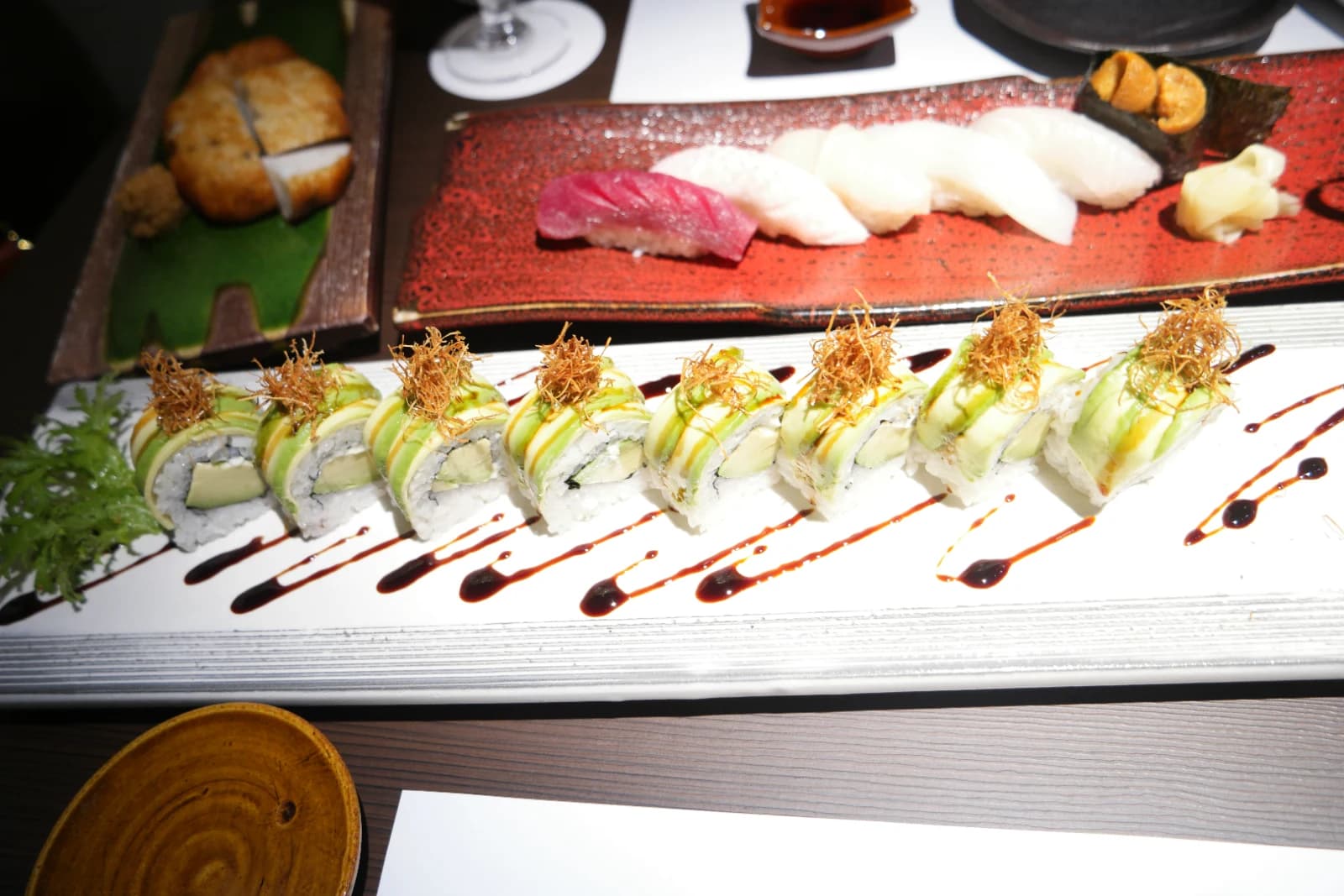Maki à l'avocat de Kurado aligné sur longue assiette blanche, rouleaux verts garnis de tempura croustillante