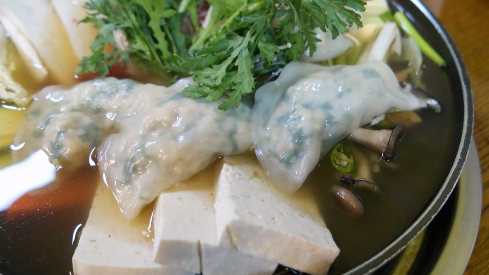 Close-up of handmade dumplings in mandu jeongol — translucent wrappers over tofu and shiitake mushrooms in soy broth