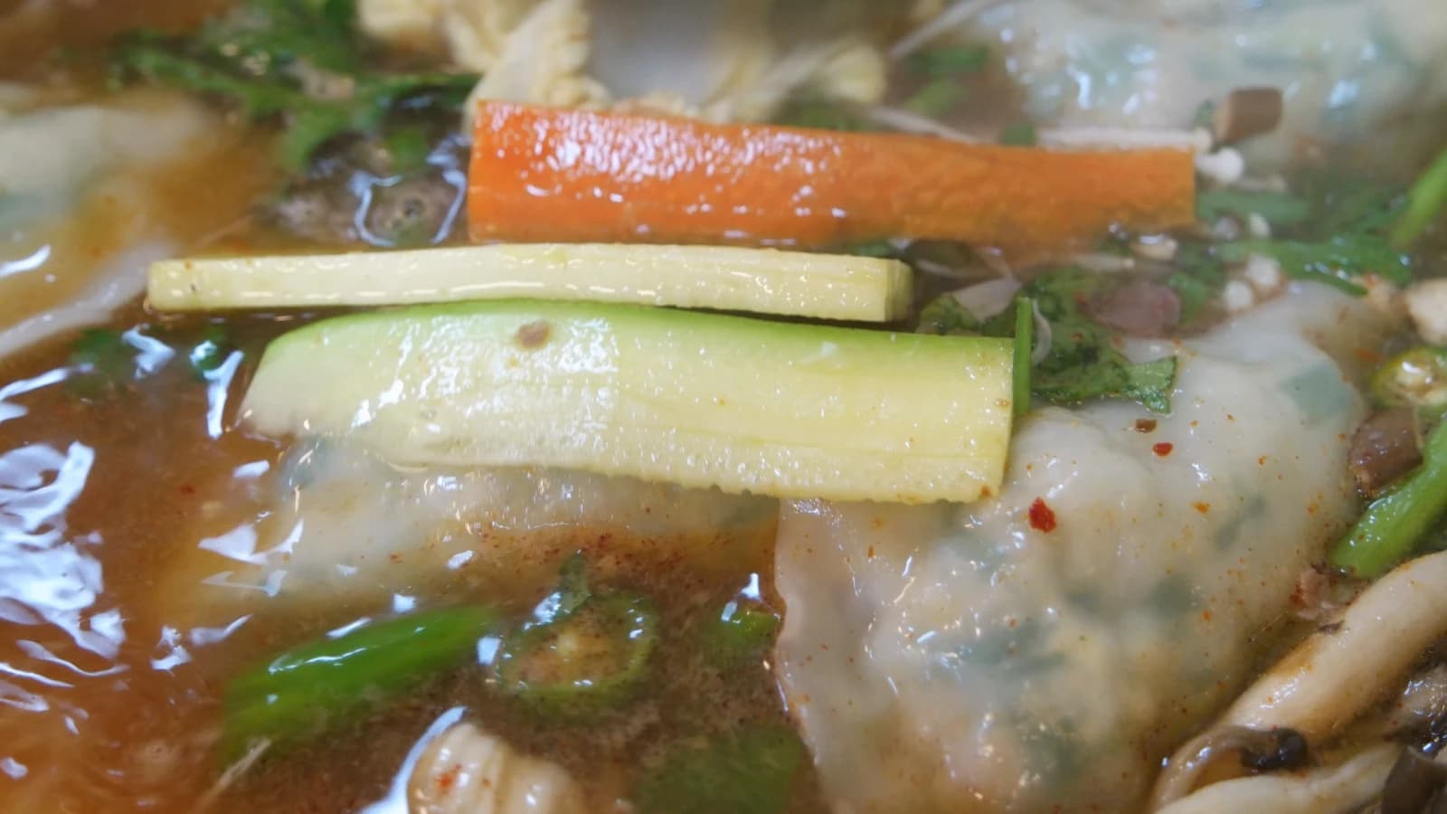 Close-up of mandu jeongol broth — tender zucchini and carrots floating in deeply concentrated soy broth