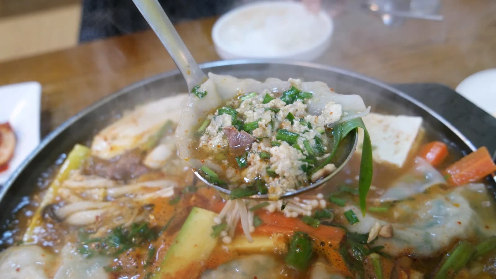 Burst dumpling on a ladle — torn wrapper with filling spilling out over the rich hot pot broth