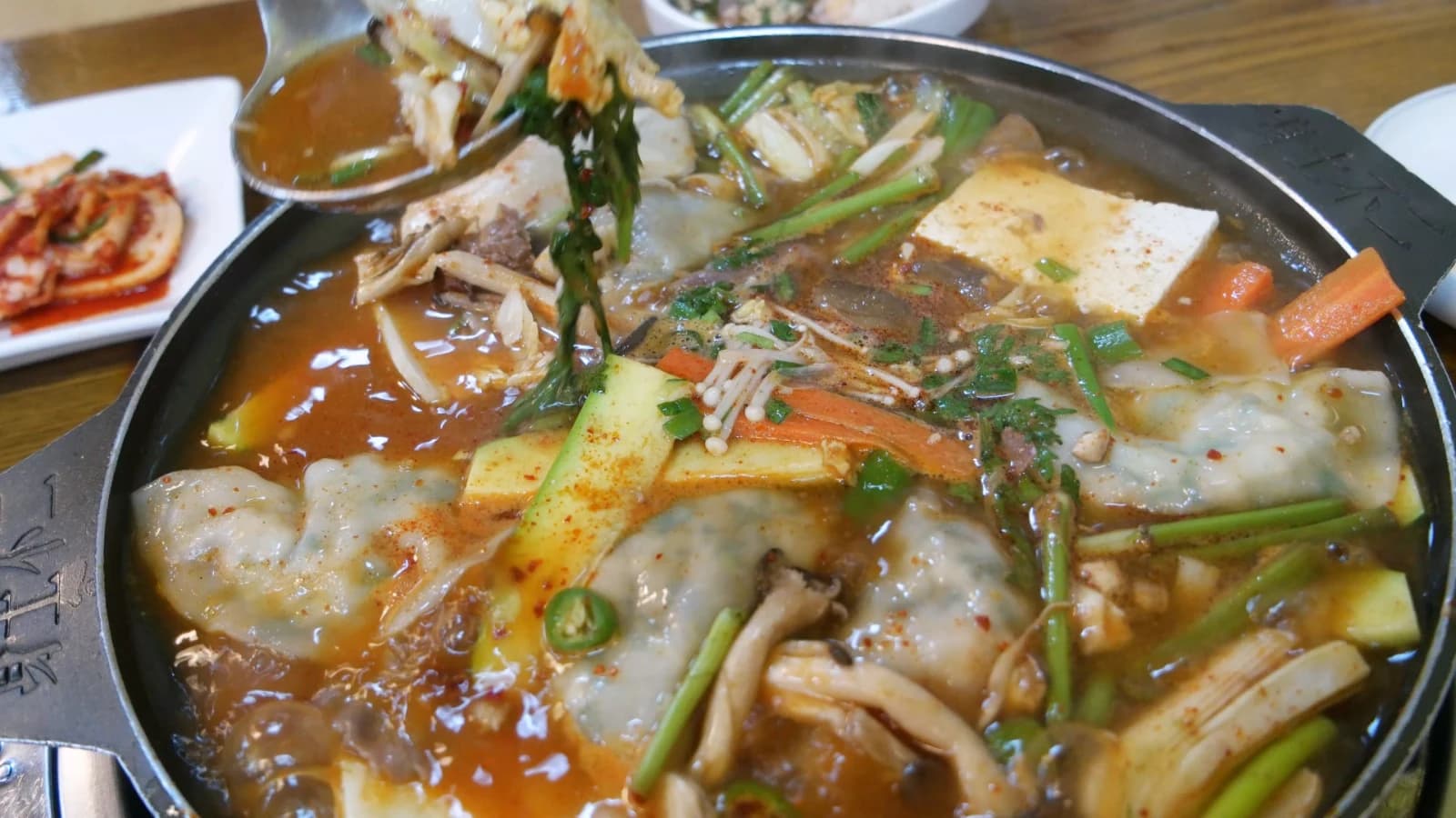 Long-simmered mandu jeongol — ingredients fully broken down in thick, dark brown broth with red pepper flakes on top