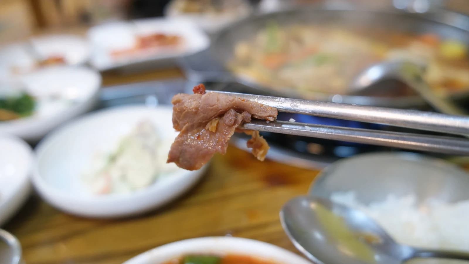 Beef from mandu jeongol — chopsticks holding a tender brown slice of beef lifted from the simmering broth
