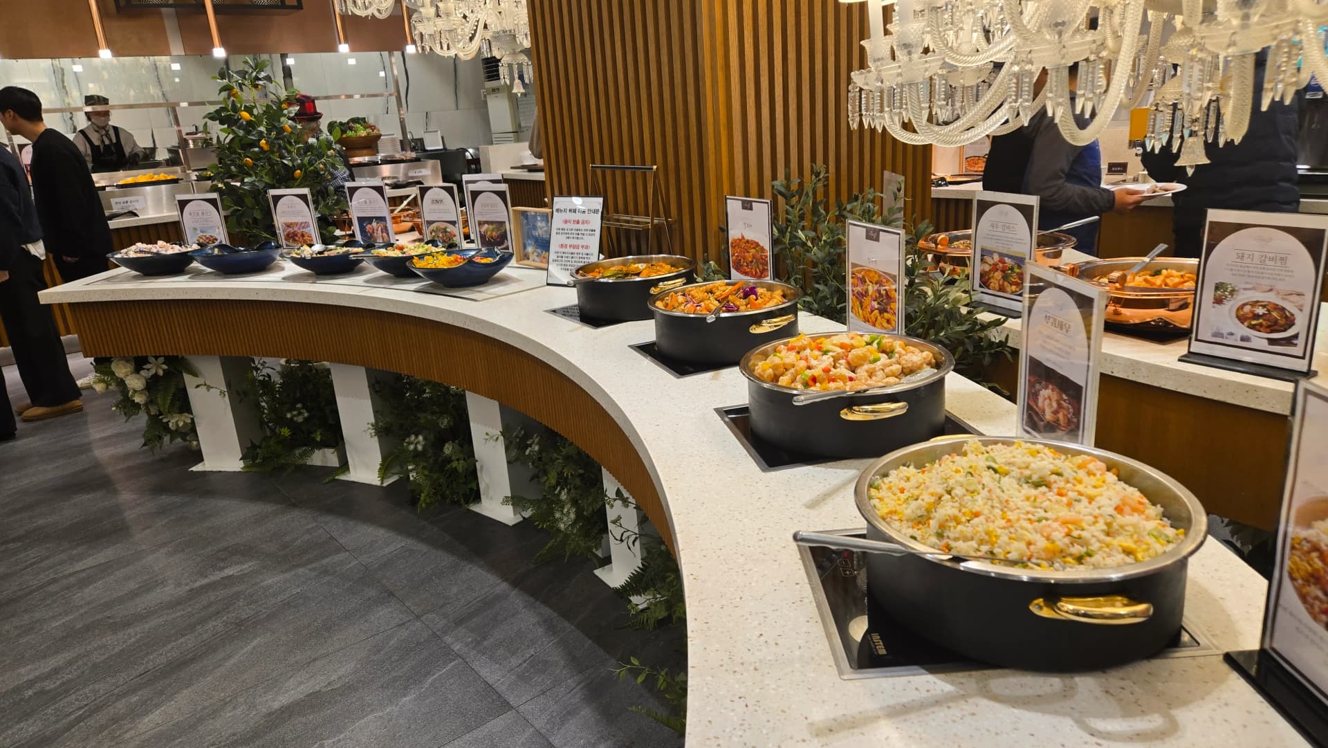 Mwonekano mzima wa buffet ya harusi ya Korea, meza zilizo na mviringo na vyakula vingi chini ya taa za chandelier | 하이제이에스비