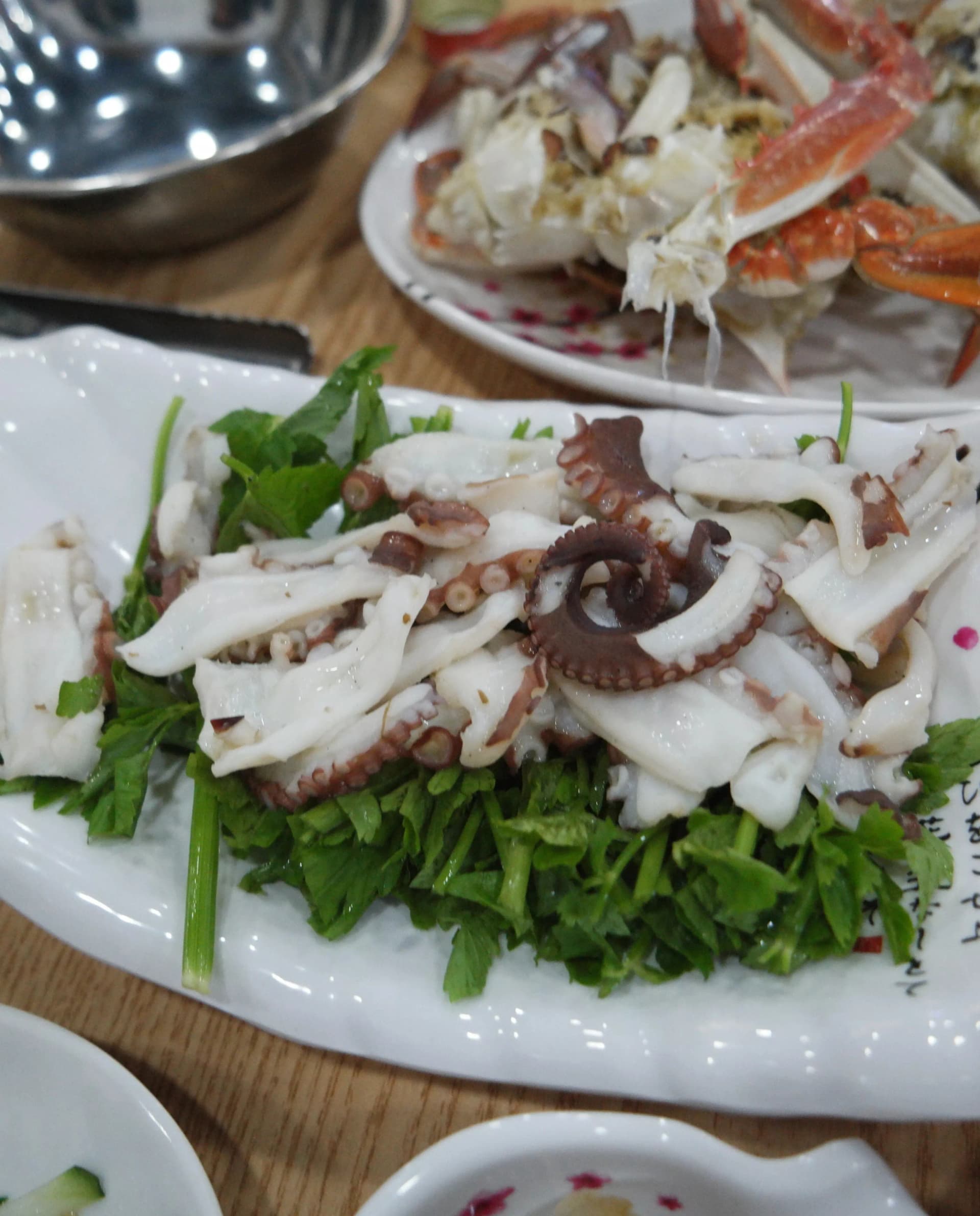 Варен калмар върху воден магданоз, а отзад се вижда син рак на пара | 하이제이에스비