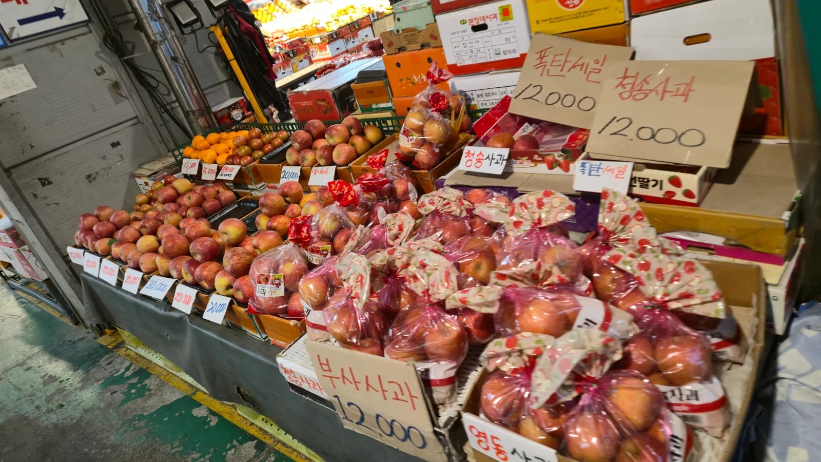 한국 전통시장에 산지별로 봉지째 쌓여 있는 청송사과 부사사과 영동사과, 한 봉지 12000원 가격표