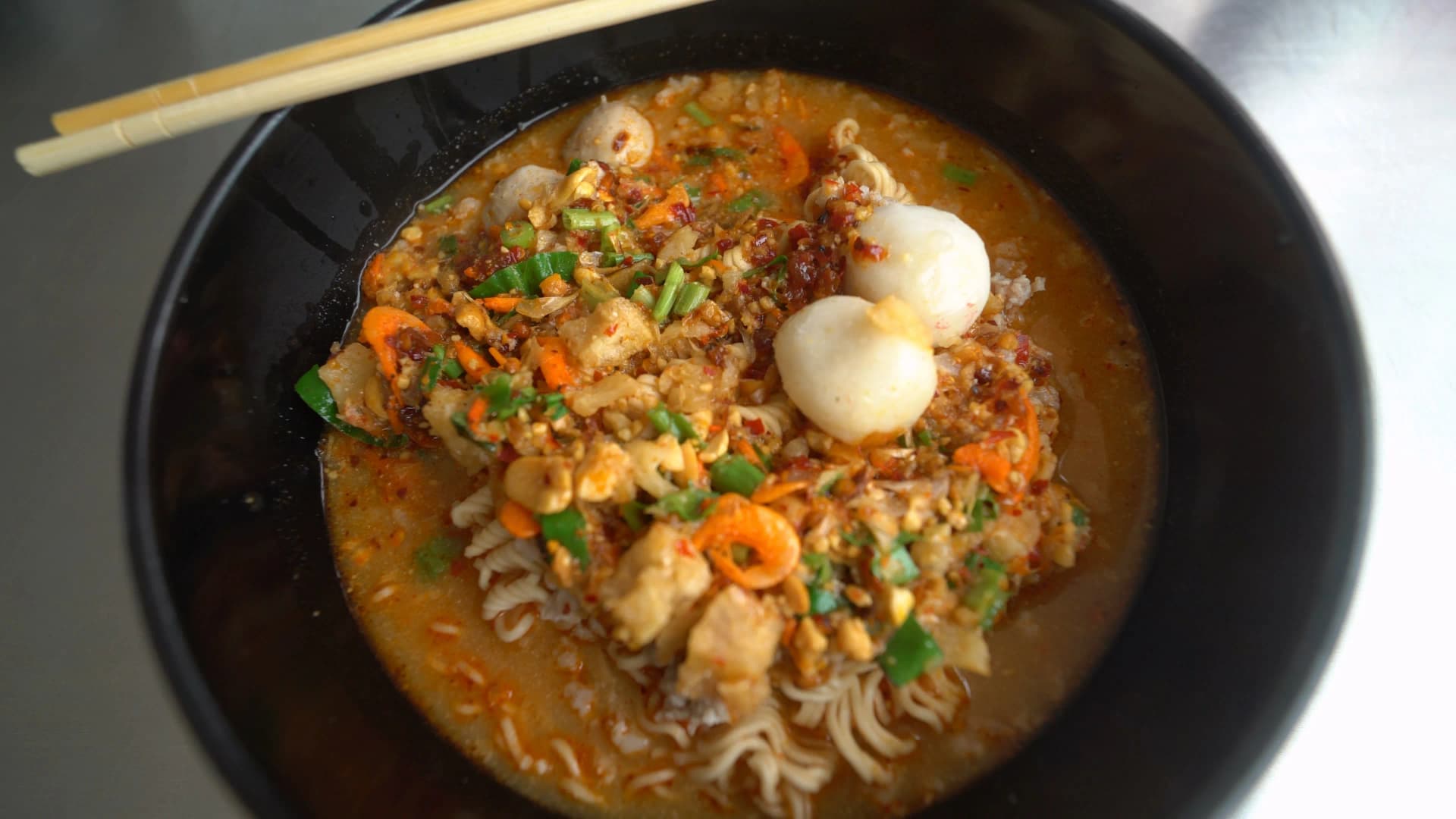 Thai tom yum mama noodles with fish balls sliced pork and chilli oil in spicy broth