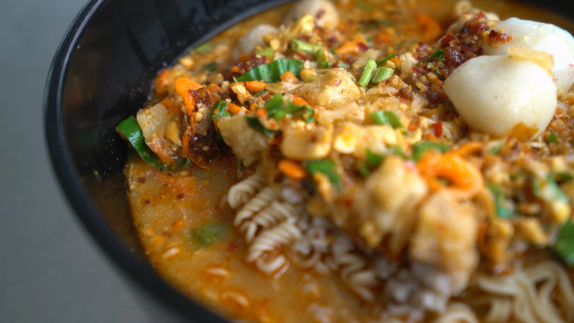 Close-up of tom yum mama noodles showing red broth crushed peanuts spring onions and dried shrimp