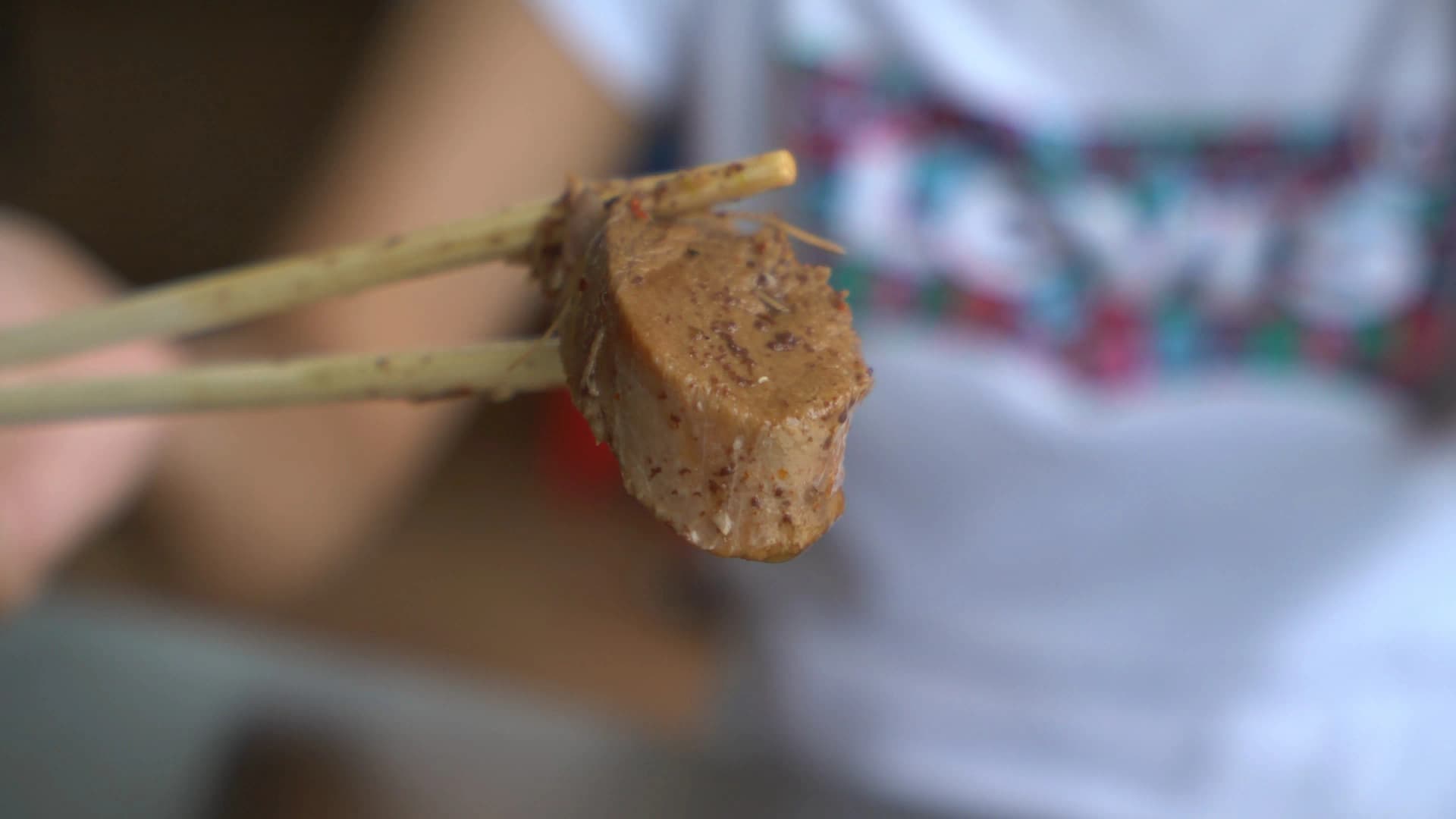 Chopsticks lifting tender shredded pork from kuay tiew nam tok blood noodle soup showing pulled texture