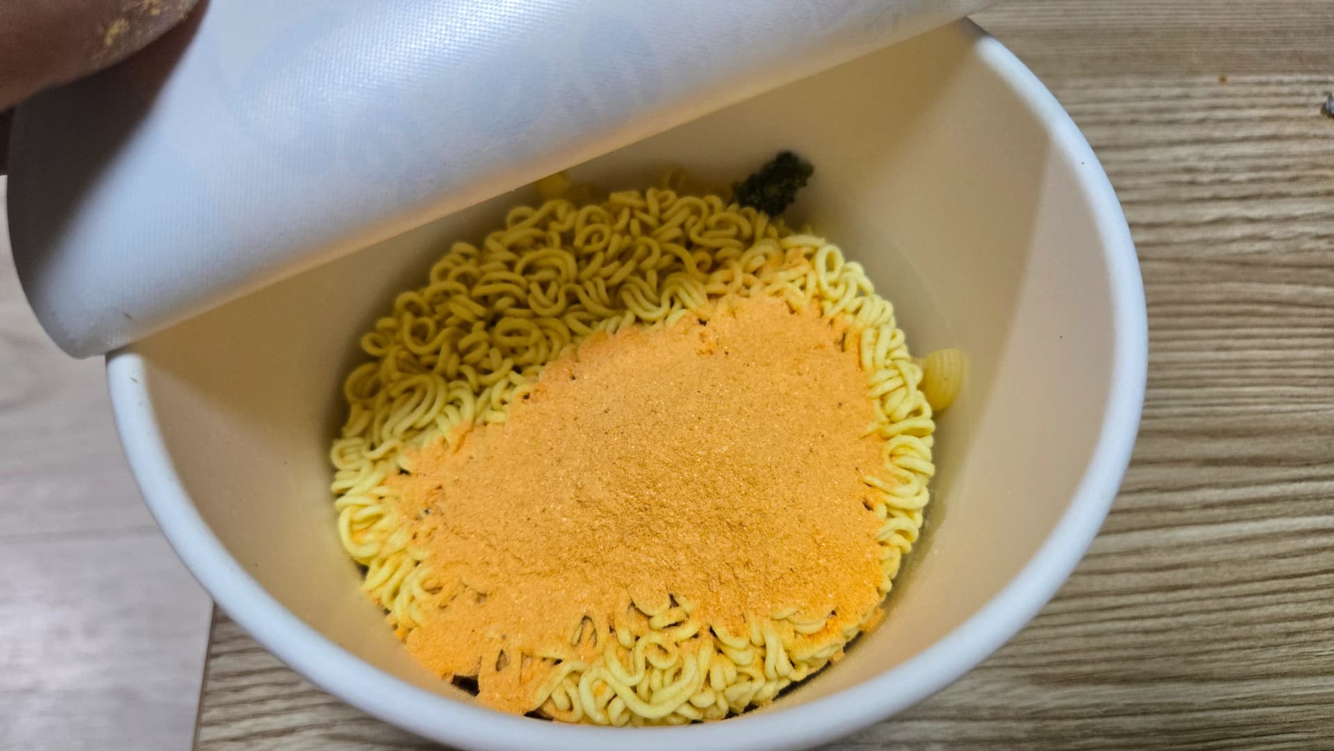 Sopa en pols de l’Ottogi Real Cheese Ramen escampada sobre els fideus — pols ataronjada acumulada sobre fideus grocs | 하이제이에스비