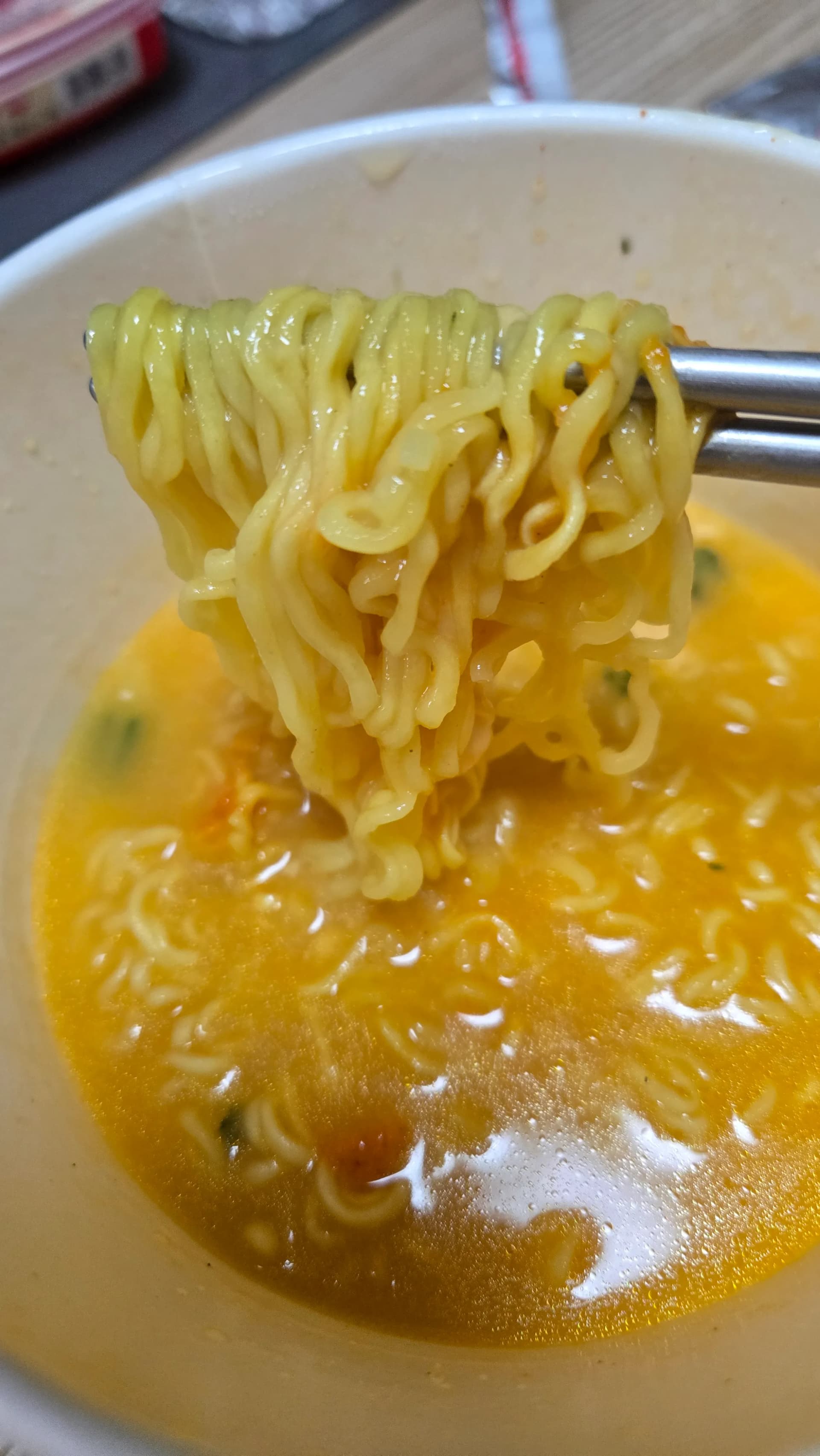 Ramen de formatge d’Ottogi ja acabat — fideus aixecats amb escuradents en un brou groc i cremós | 하이제이에스비