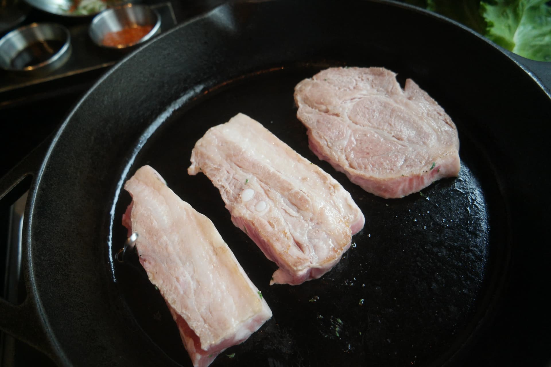 Fetta di samgyeopsal sul punto di essere girata con il lato ancora crudo che inizia a sbiancarsi | 하이제이에스비