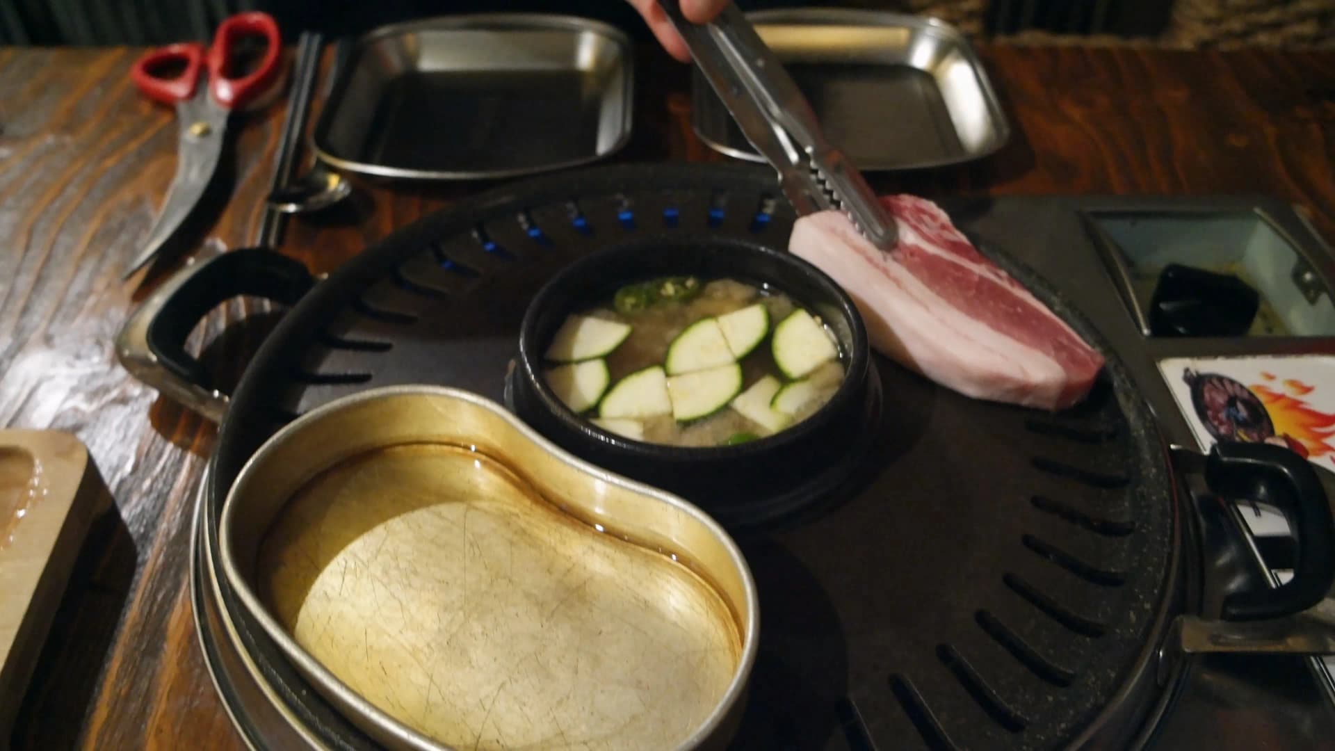 집게로 두툼한 생삼겹살을 불판 위에 올리는 장면 | 하이제이에스비