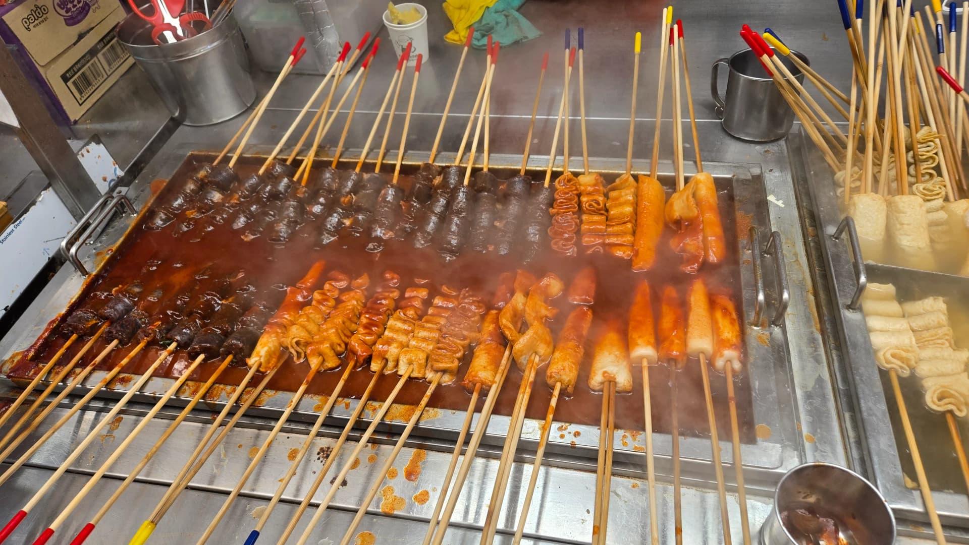 Nahaufnahme der Gochujang-Reiskuchen-Spieße — tief in rote Gochujang-Soße getauchte Tteok-Spieße | 하이제이에스비