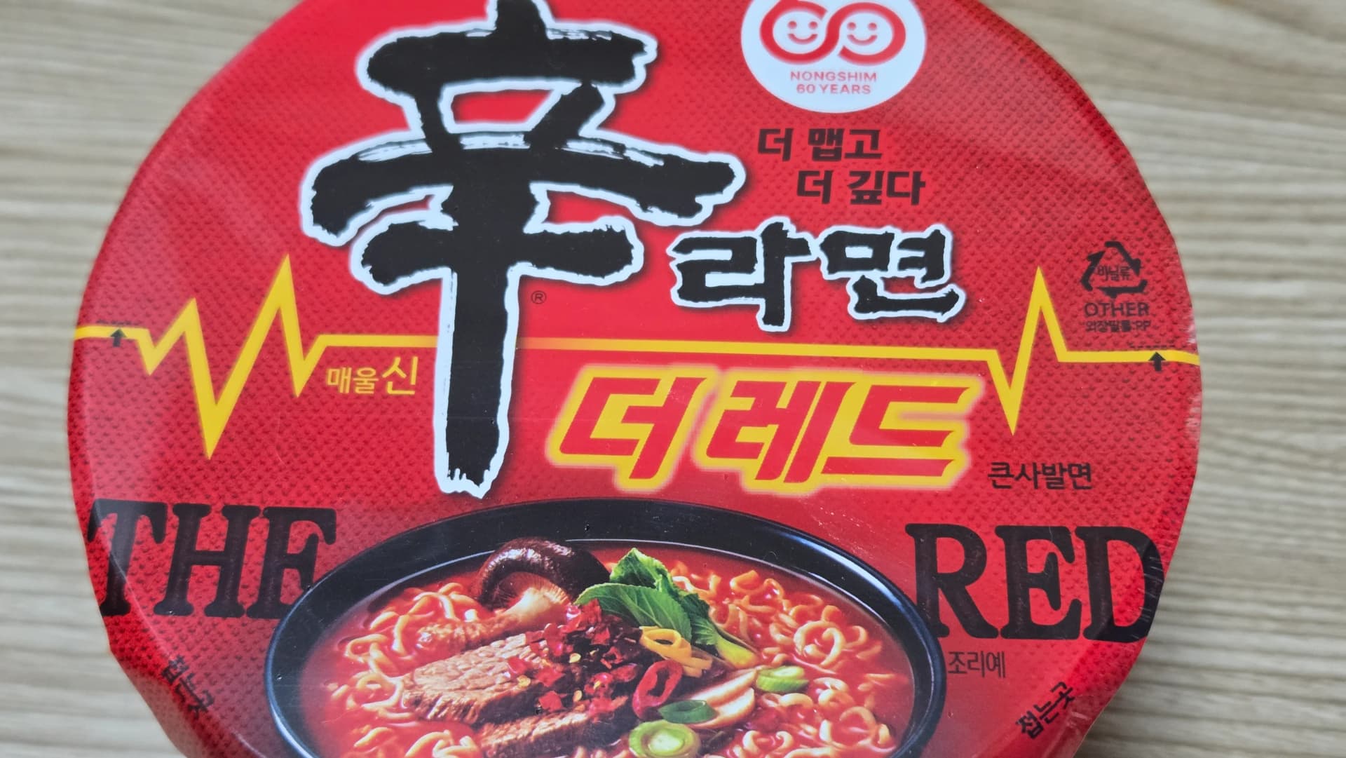 Coperchio del cup noodle Shin Ramyun The Red in primo piano con scritta più piccante più profondo e linea gialla a elettrocardiogramma