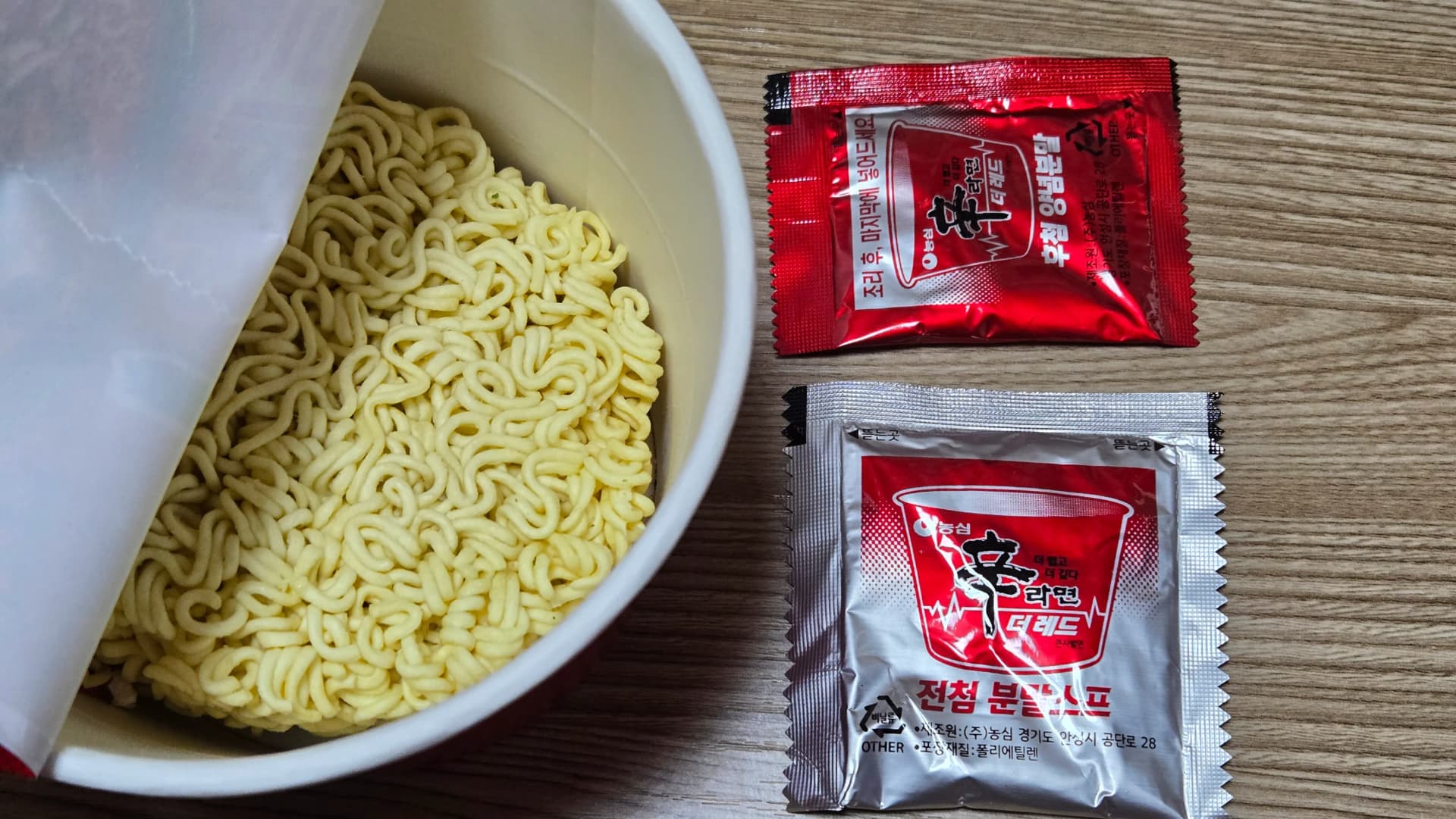 Contenuto del cup noodle Shin Ramyun The Red aperto con noodle e due bustine di condimento