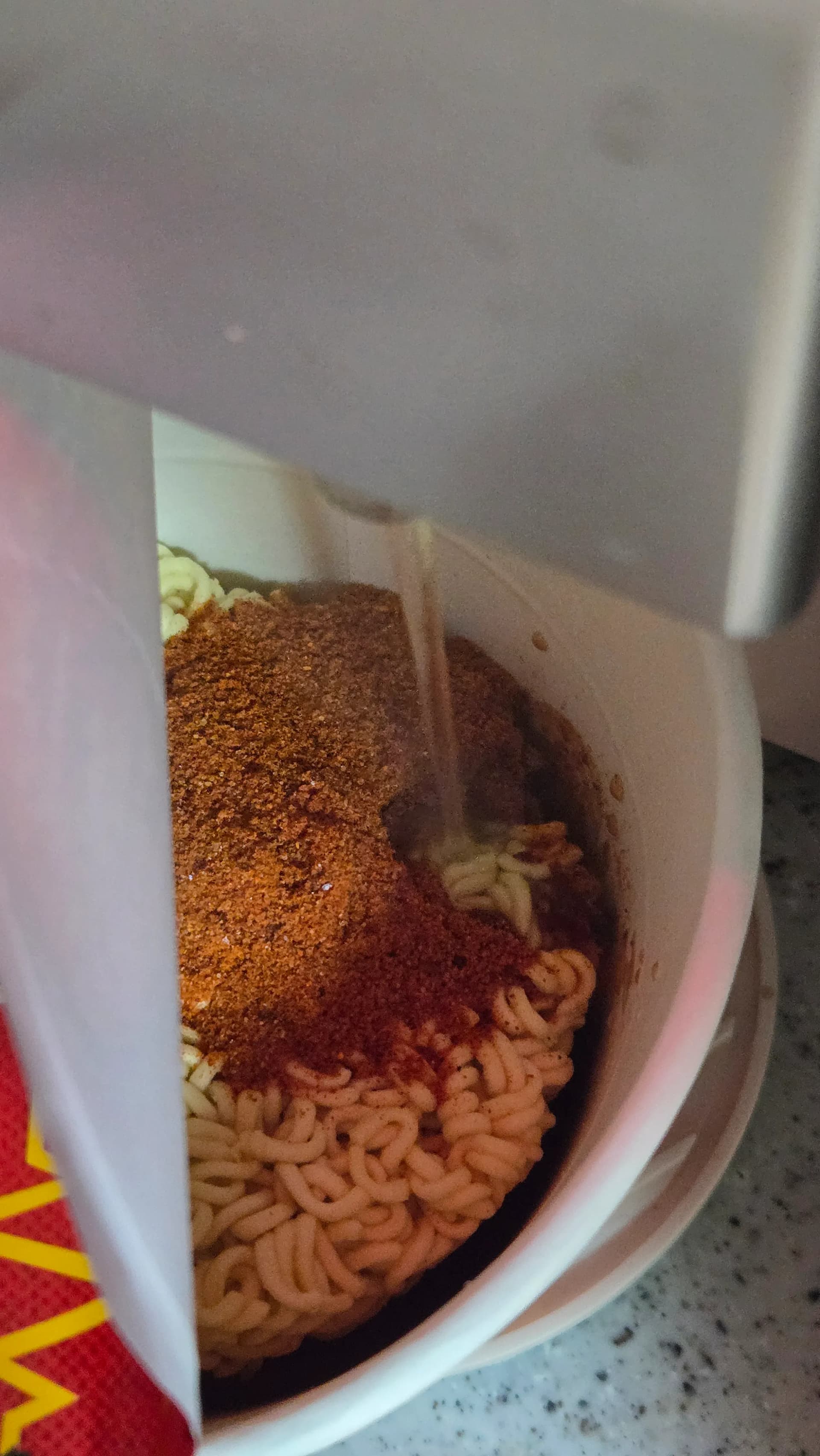 Preparazione del ramen piccante Shin Ramyun The Red con polvere base rossa sui noodle e acqua bollente versata