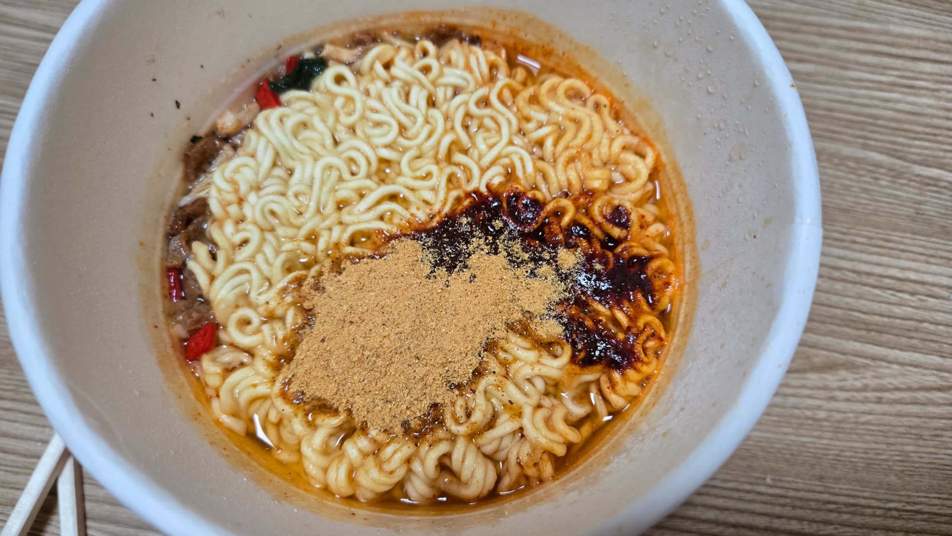 Condimento piccante in polvere marrone versato sopra i noodle dello Shin Ramyun The Red cup