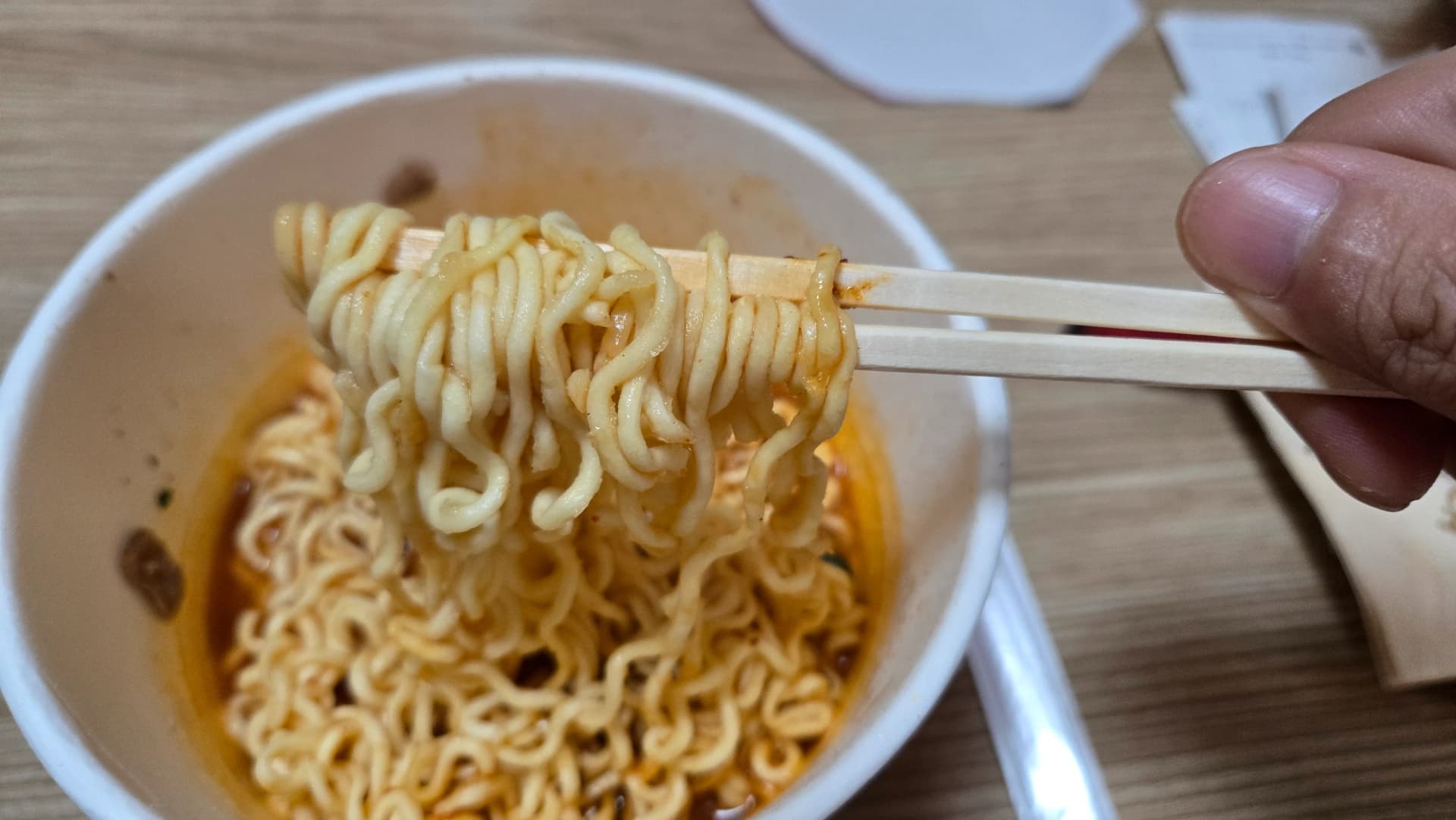 Noodle spessi dello Shin Ramyun The Red sollevati con le bacchette con brodo rosso che gocciola