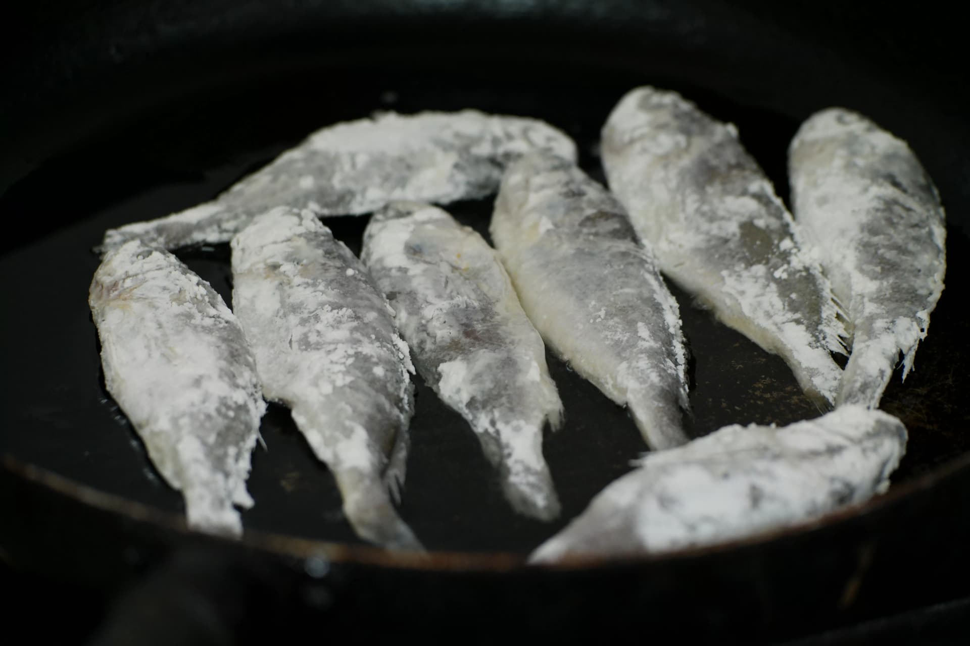 Flour-dusted croaker sizzling in oil on a dark frying pan during the Korean pan-frying process