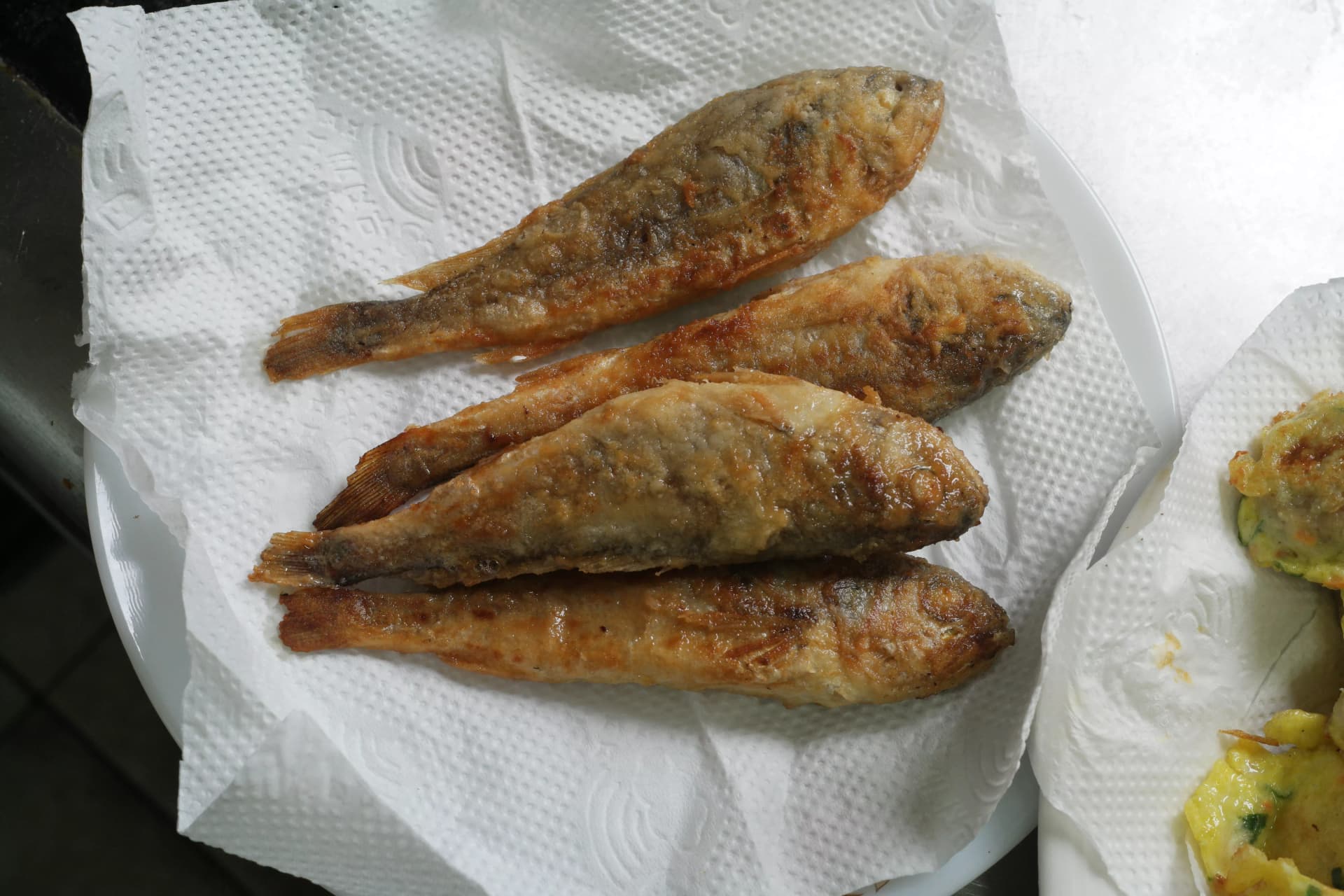 Three golden pan-fried croaker resting on kitchen paper towel with excess oil draining off