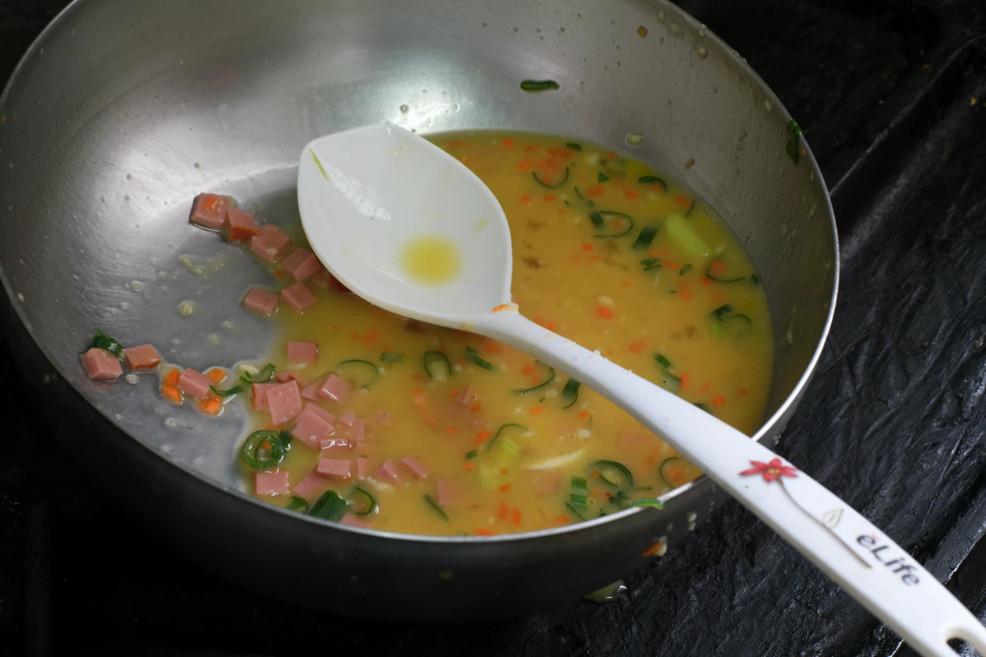 Stainless steel bowl with beaten egg mixture containing diced ham, spring onion, and carrot for Korean rolled omelette