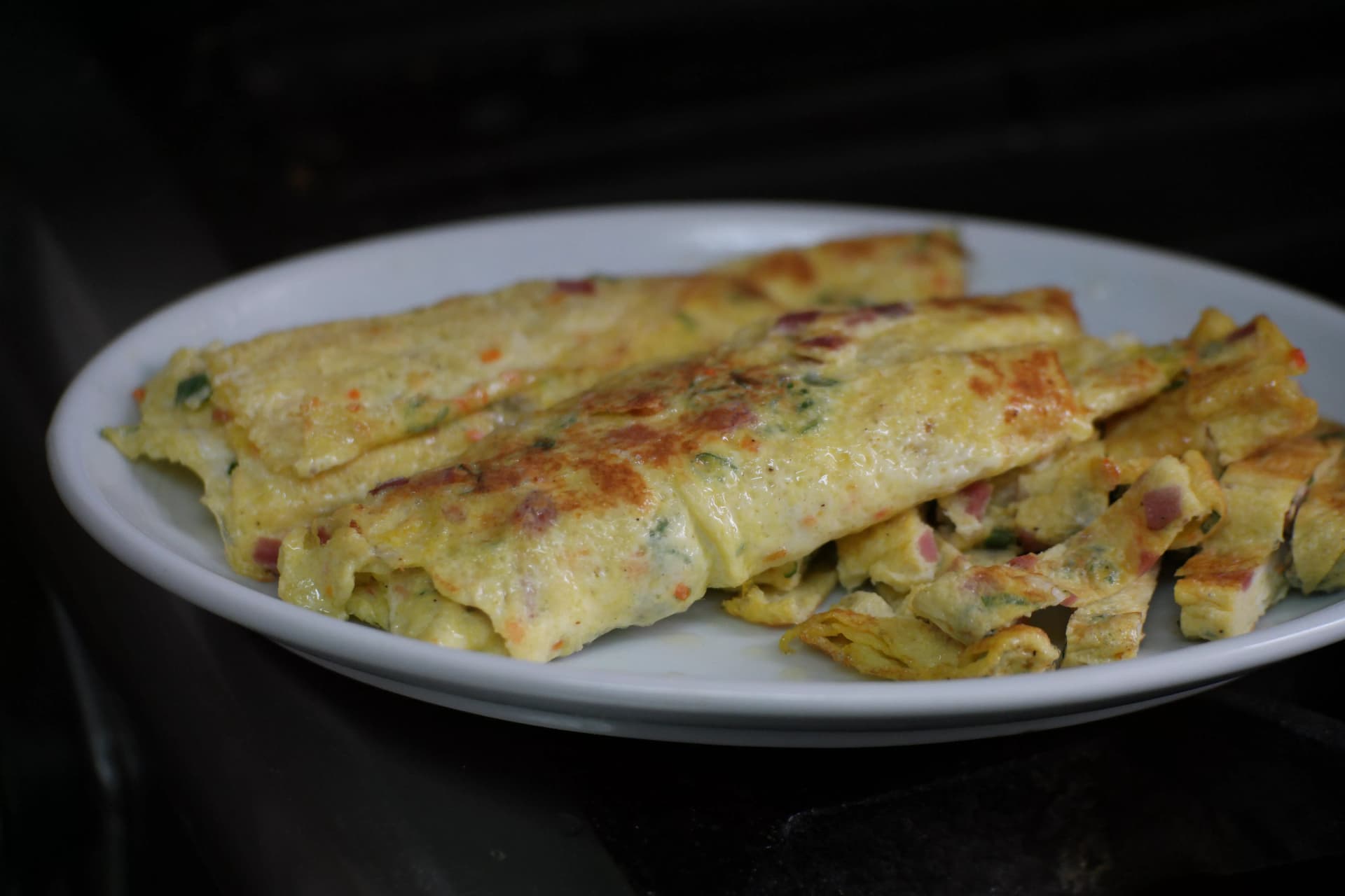 Finished Korean rolled omelette sliced and arranged neatly on a plate with ham and spring onion visible in each piece