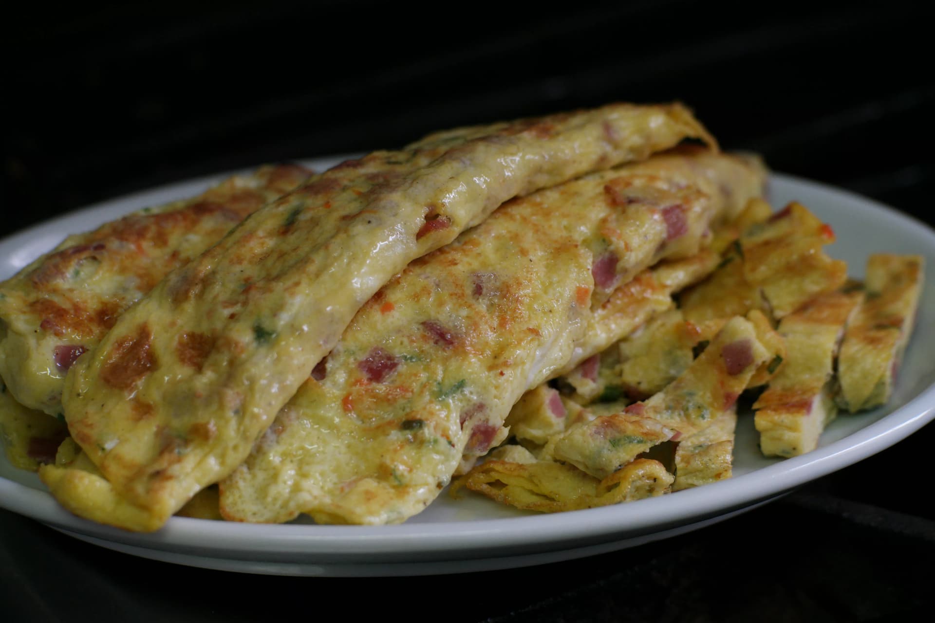 Close-up of gyeran-mari cross-section showing golden exterior and colourful filling of ham, egg, and spring onion