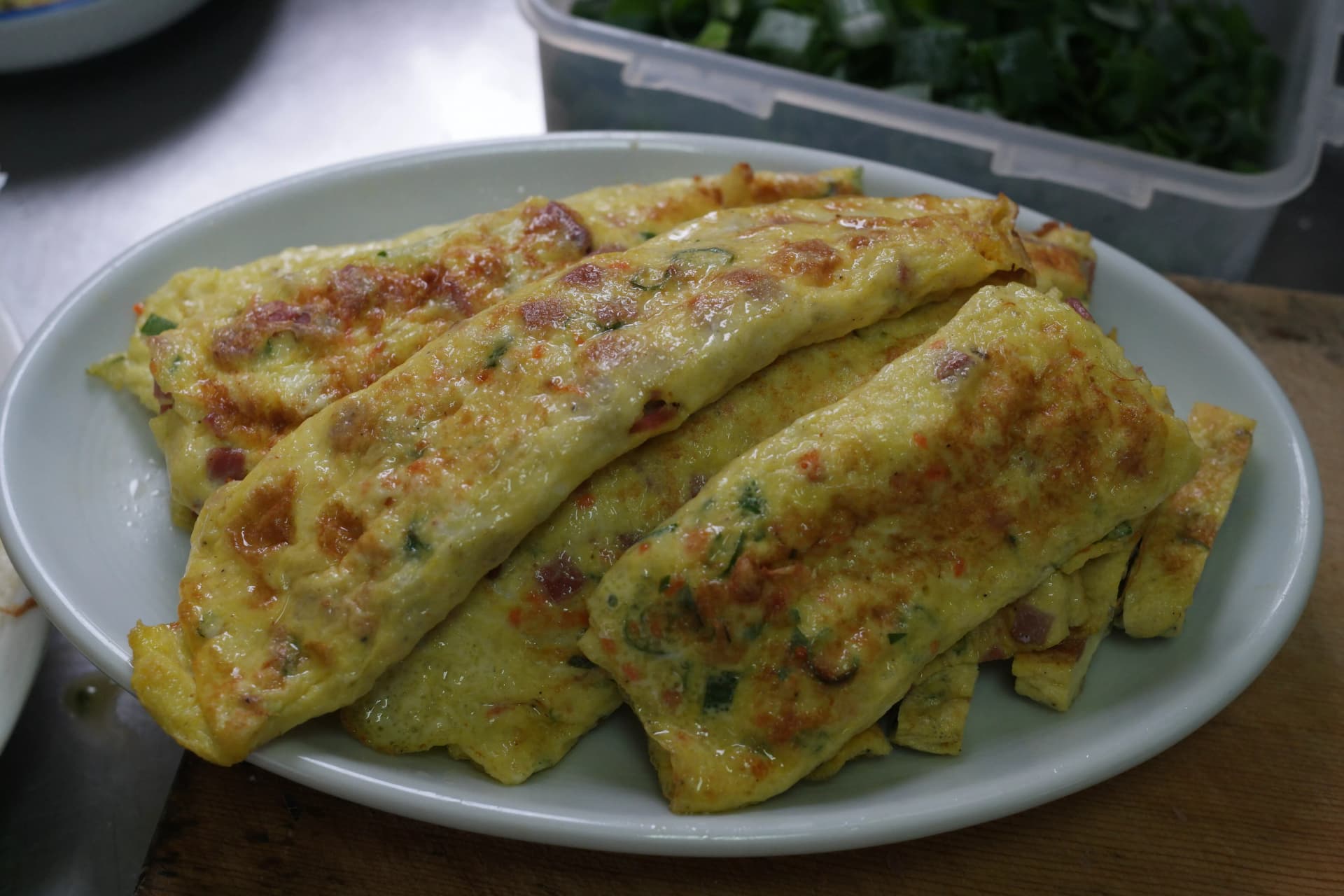 Plate of Korean rolled omelette on the canteen prep bench with chopped vegetables for the next dish in the background