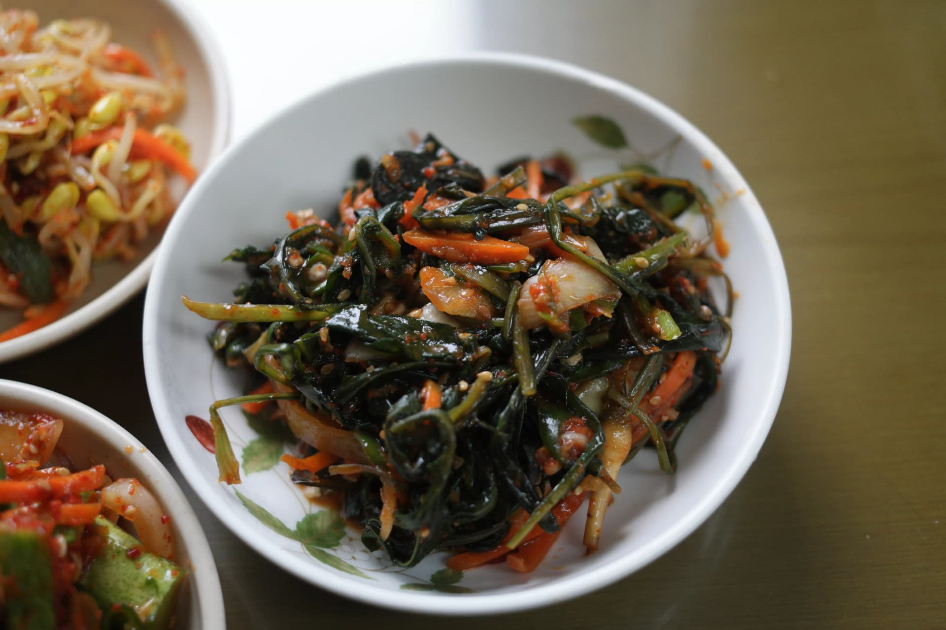Dark green seasoned Korean vegetable side dish with carrot and sesame seeds in soy-based dressing, possibly sweet potato stems