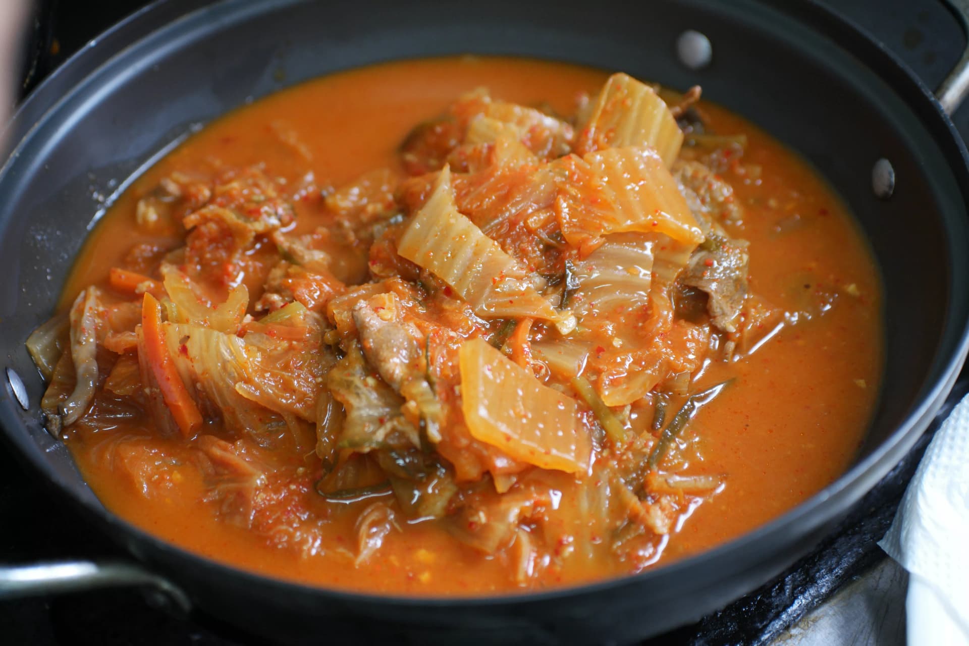 Bubbling pot of Korean kimchi stew in early cooking stage with aged kimchi and pork simmering in red broth