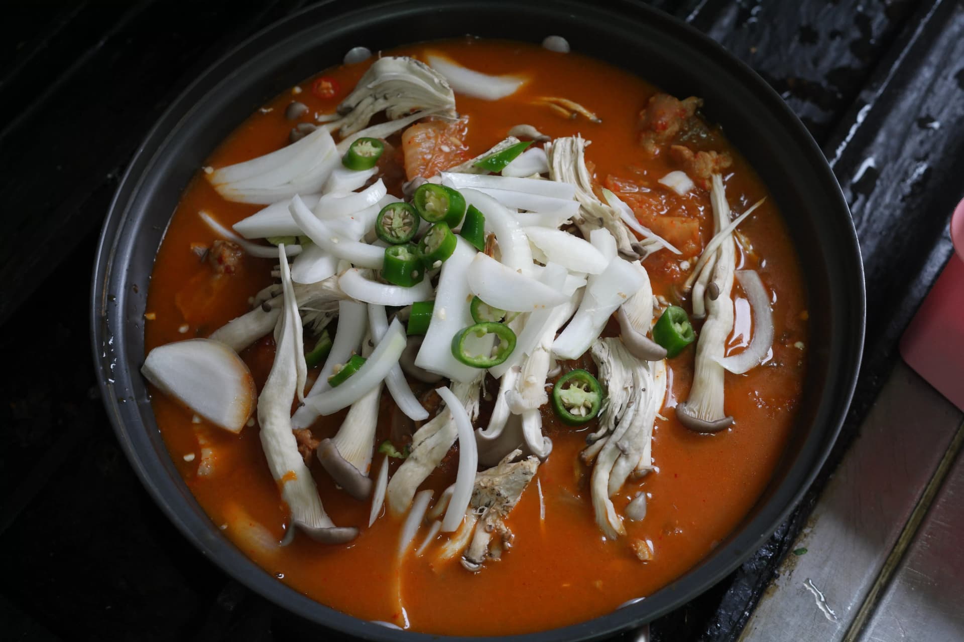 Oyster mushrooms and sliced cheongyang chilli added on top of simmering kimchi jjigae mid-cooking