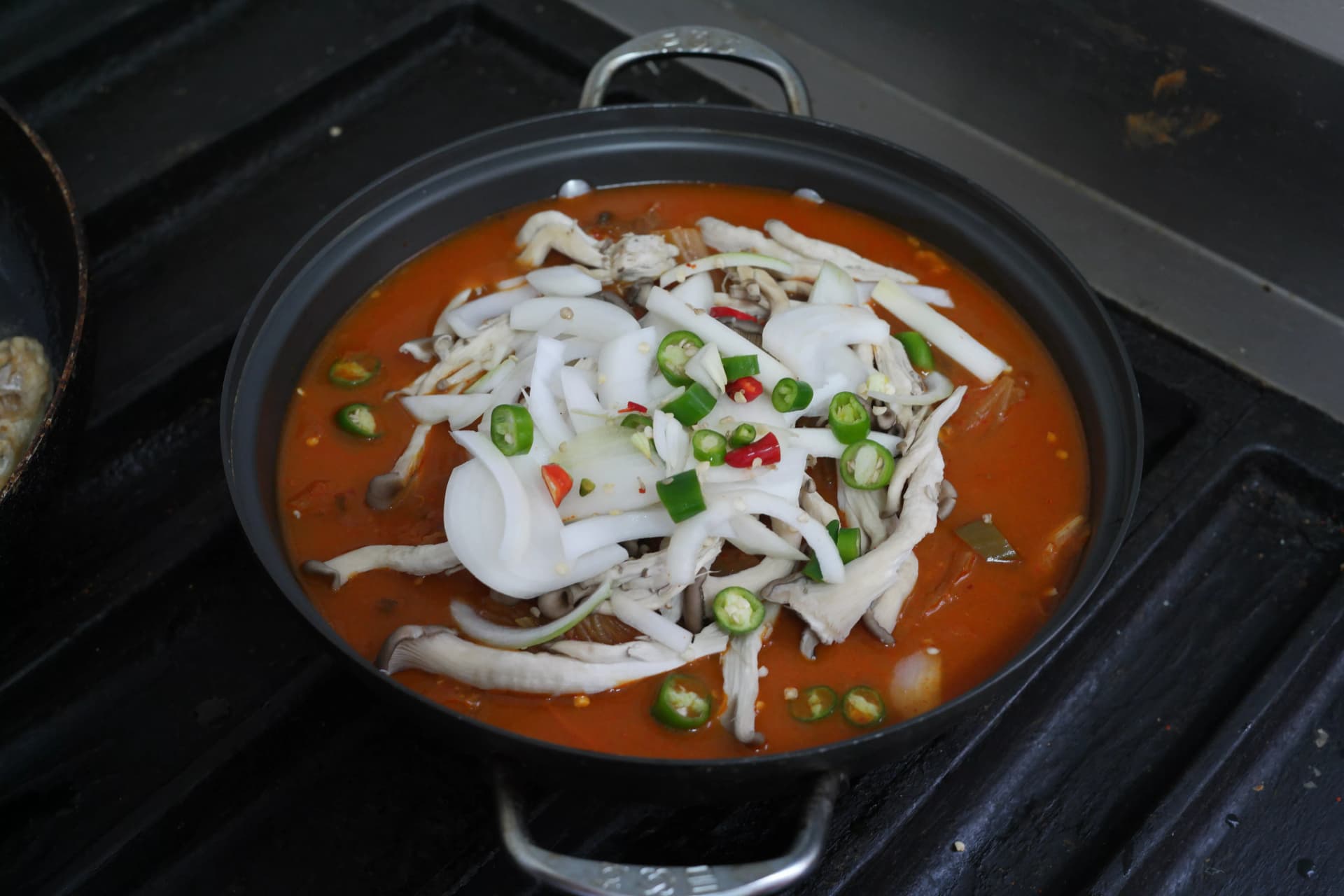 Kimchi stew pot now filled with added onion slices and mushrooms in the layered Korean cooking process