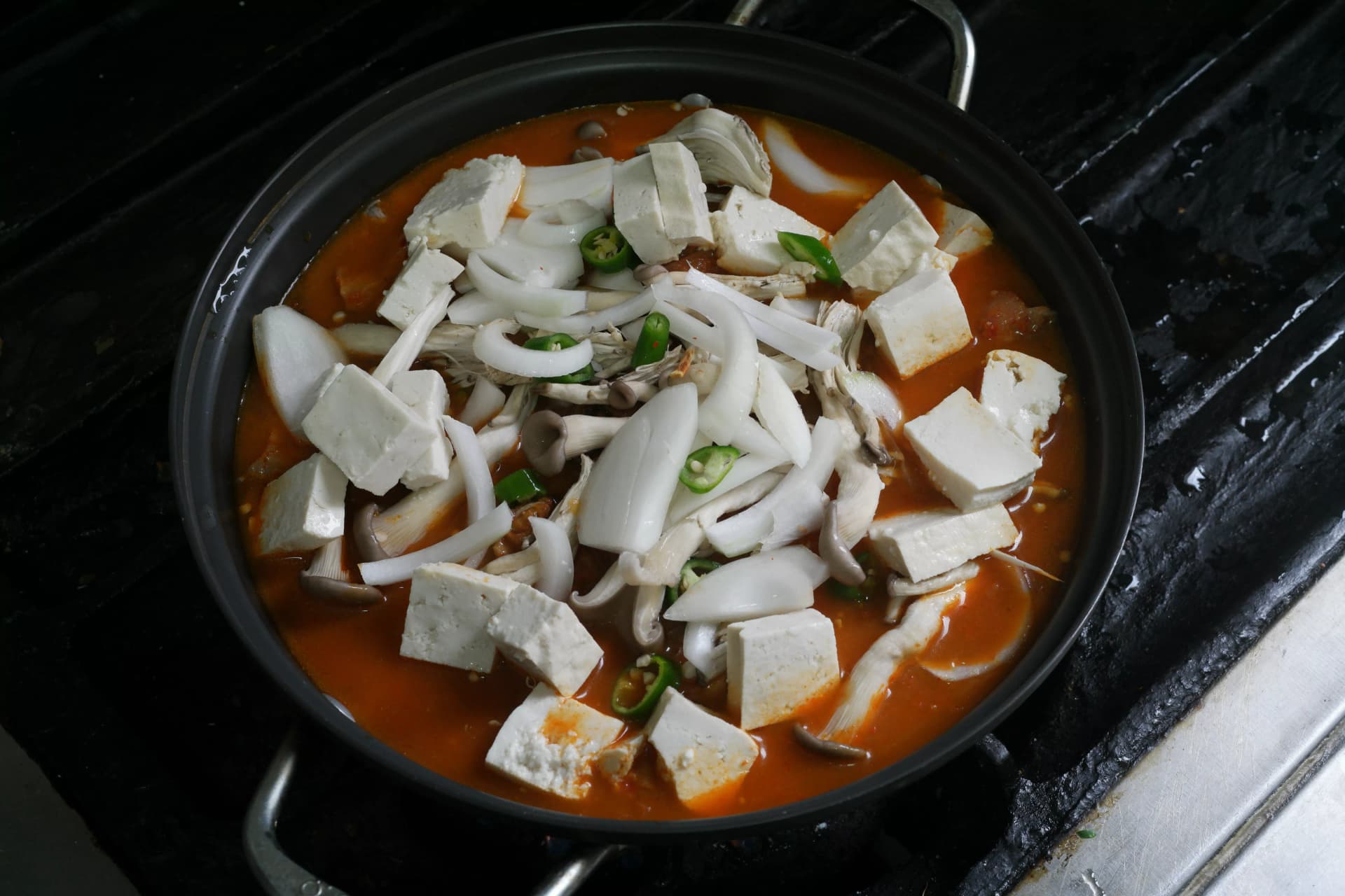 Large chunks of tofu placed on top of kimchi jjigae just before the stew is finished