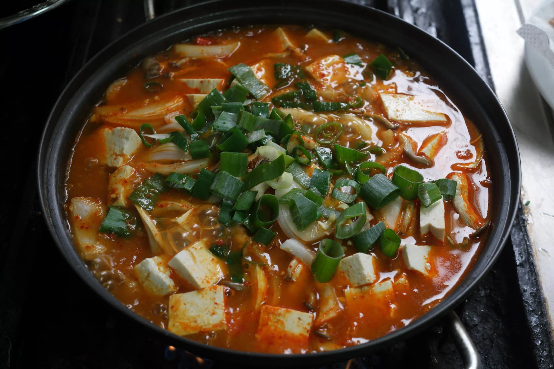 Completed kimchi jjigae bubbling vigorously in the pot topped with sliced spring onion ready to serve