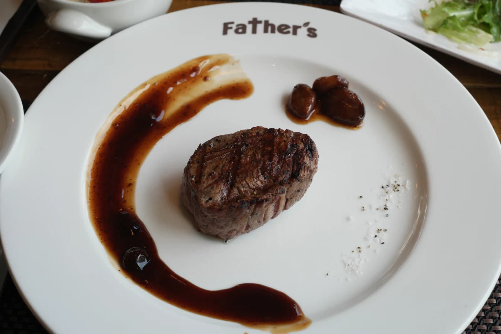 韓国ステーキ専門店のメインのヒレステーキ、皿の中央に分厚いヒレ肉が置かれデミグラスソースとローストにんにくが添えられている