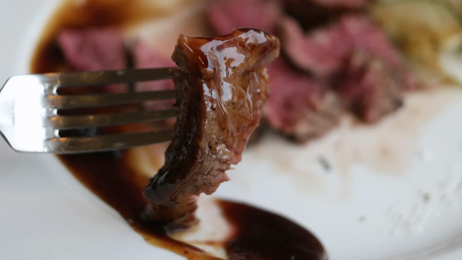 切り分けたヒレ肉をデミグラスソースにたっぷり浸けて持ち上げた様子、ソースが肉の表面を伝って滴っている