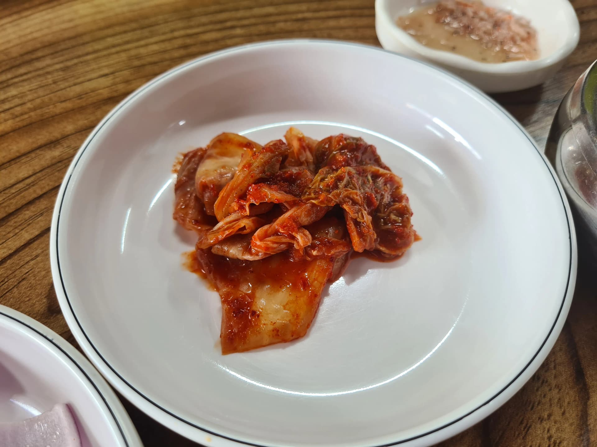 كيمتشي ملفوف صيني معتّق بلون بني غامق على صحن أبيض — مقبلة جانبية لشوربة عظم بالنقانق الكورية