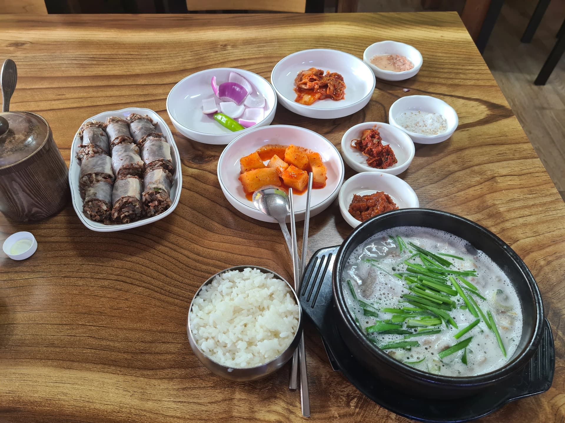 طاولة كاملة لسوندي غوكباب — طاجن شوربة فوّار وصحن أرز ستانلس وصحن سوندي ومقبلات تغطي طاولة خشبية