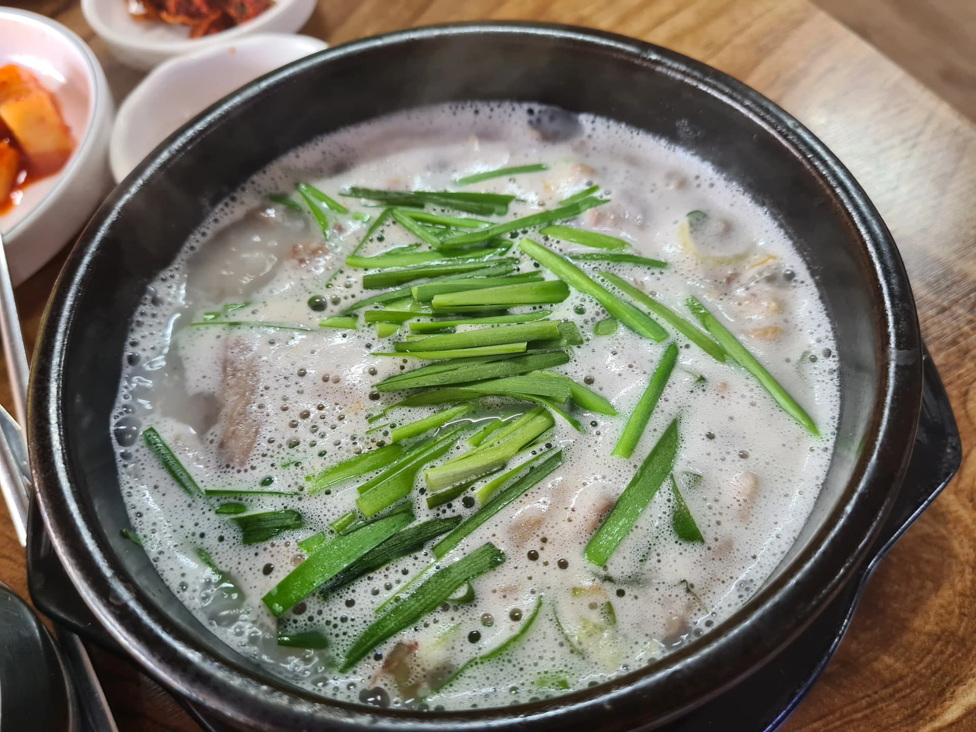 سوندي غوكباب عن قرب — مرق عظم خنزير أبيض حليبي مع ثوم معمر فوقه والسوندي والأحشاء مغمورة تحته بالطاجن الحجري