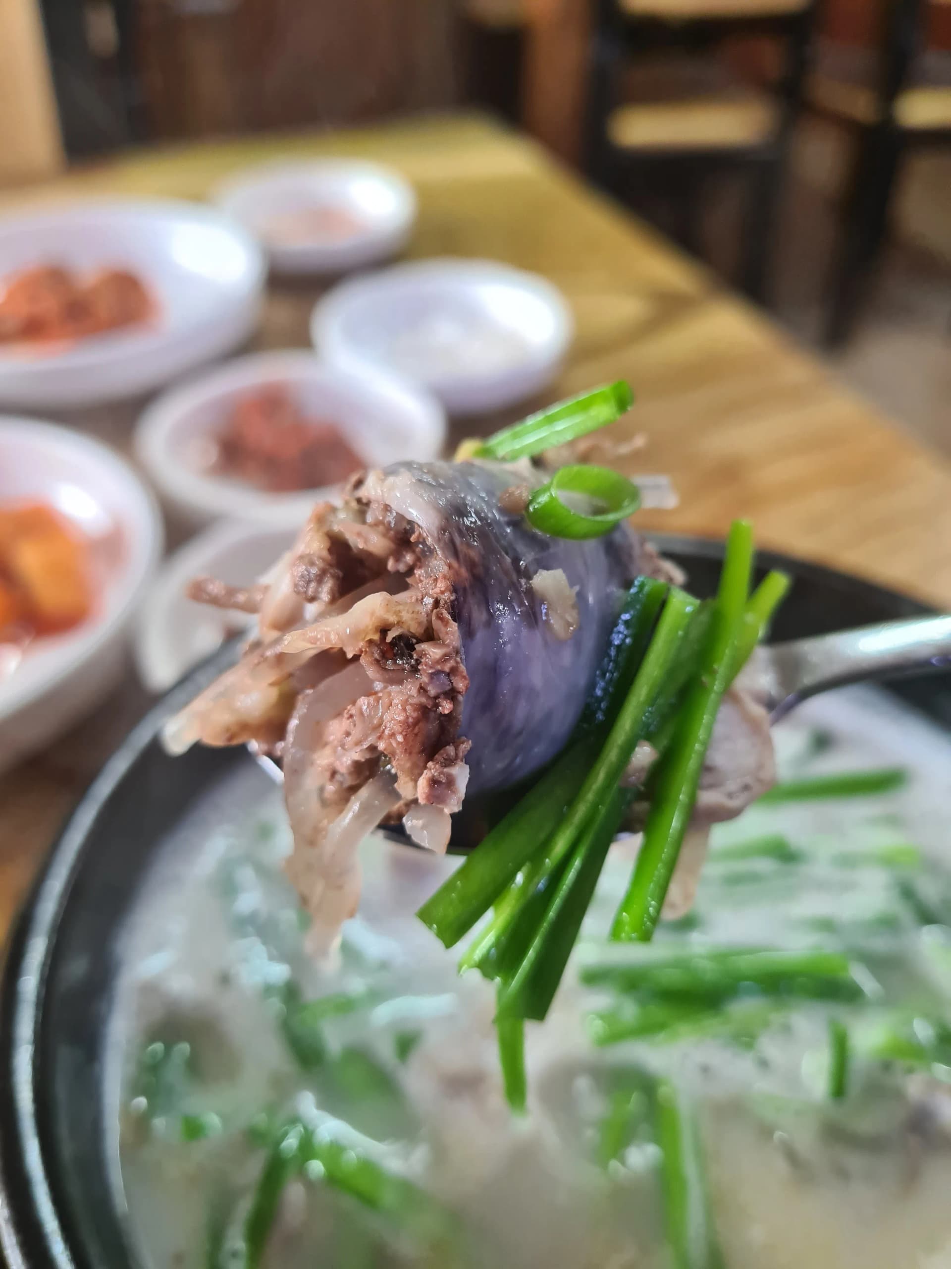 ملعقة مرفوعة من سوندي غوكباب فيها قطعة نقانق دم وثوم معمر وأحشاء بالمرق الأبيض