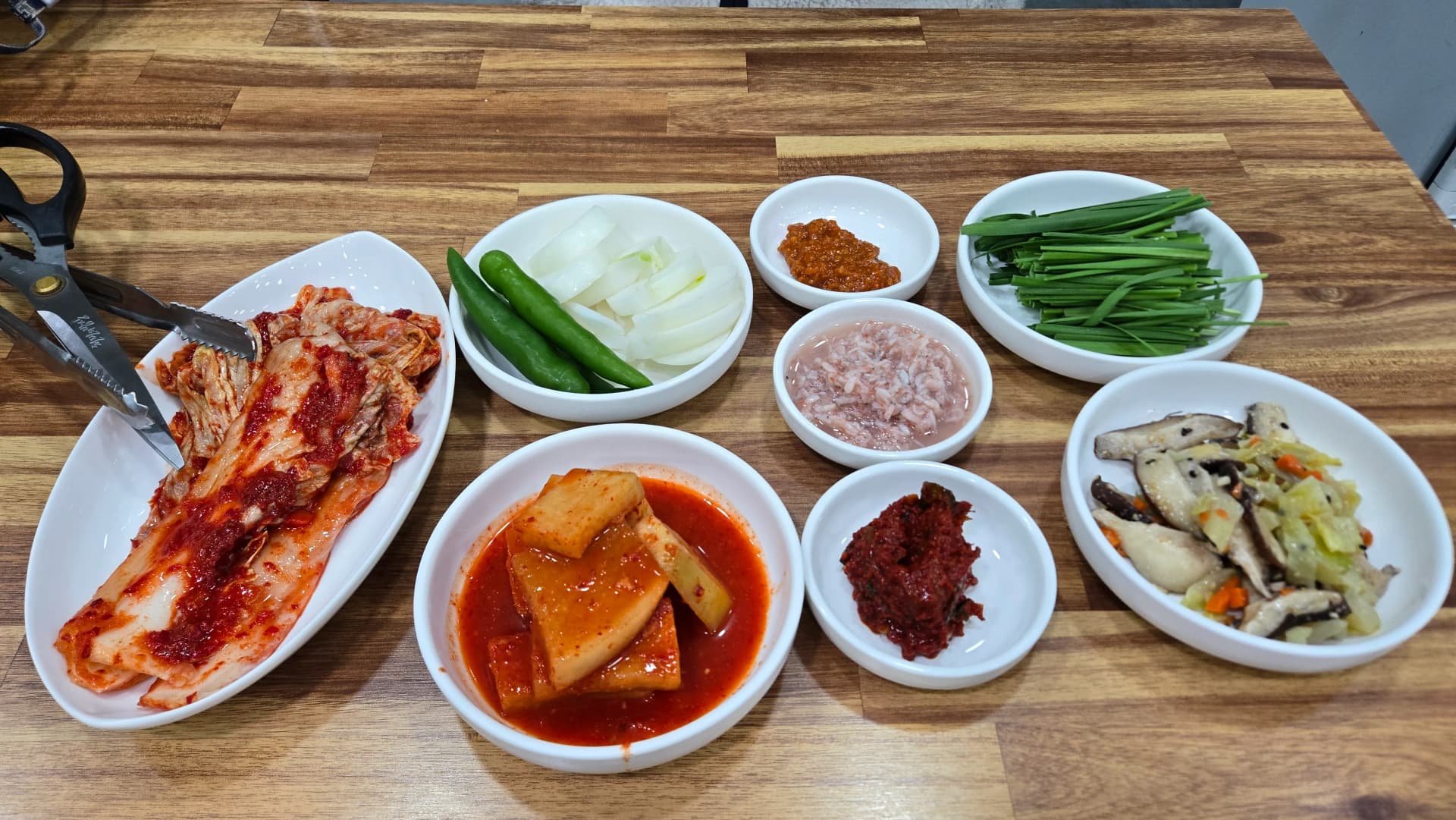 Full table spread at a local pork bone broth soup restaurant showing sundaegukbap dwaeji-gukbap kimchi radish pickles onion chilli peppers and fermented shrimp on a wooden table