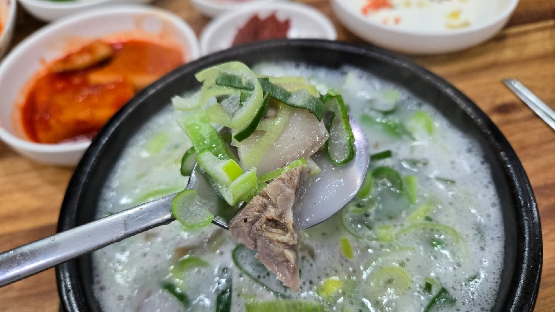 Stirring sundaegukbap with a spoon revealing blood sausage boiled pork and offal hidden beneath the broth