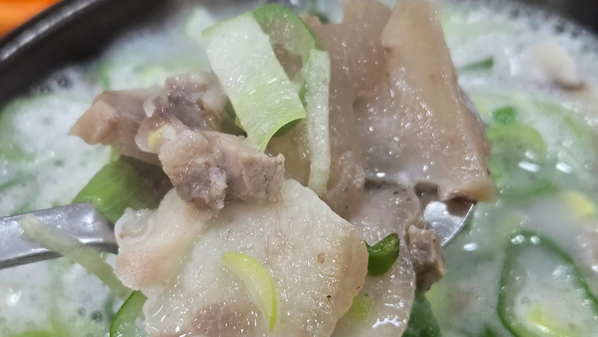 Sliced boiled pork belly with skin on showing chewy texture inside the pork bone broth soup