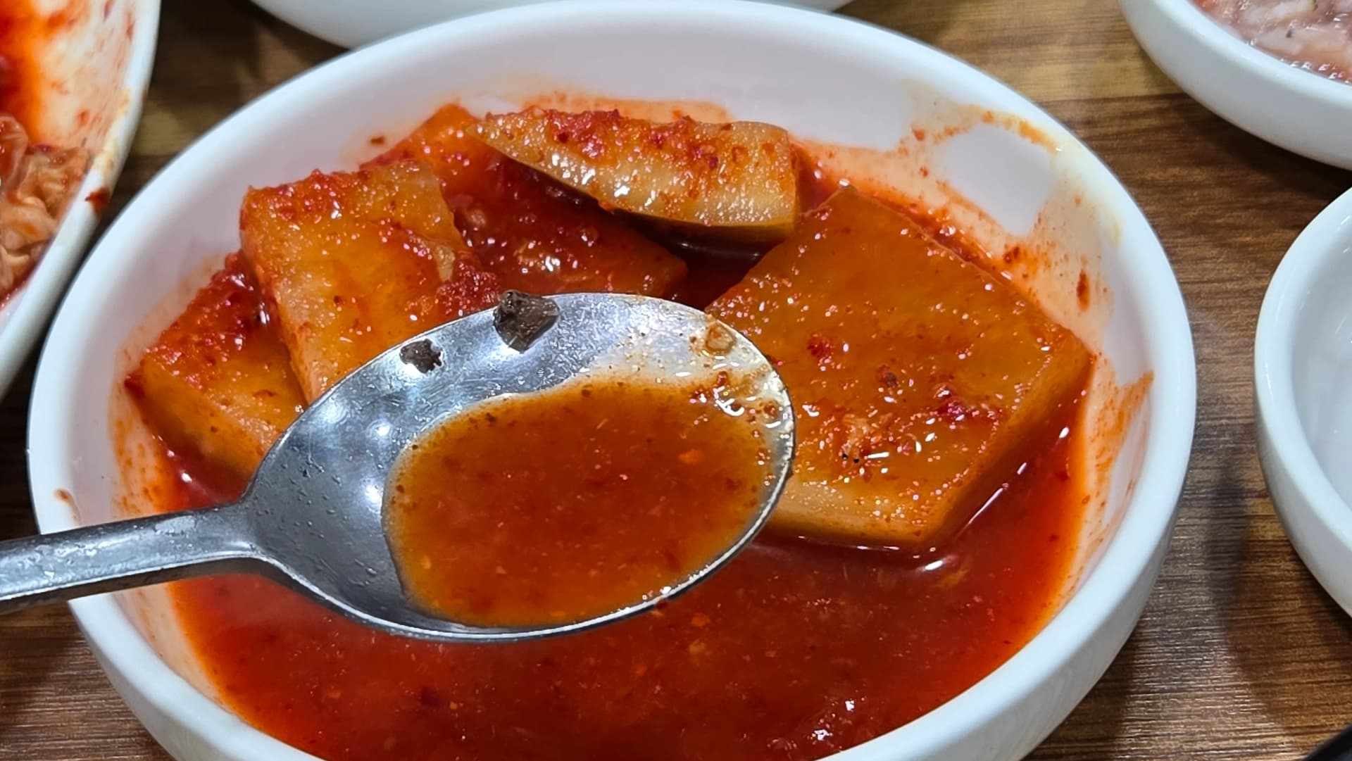 Spooning tangy kkakdugi radish kimchi juice into a bowl of sundaegukbap to add flavour