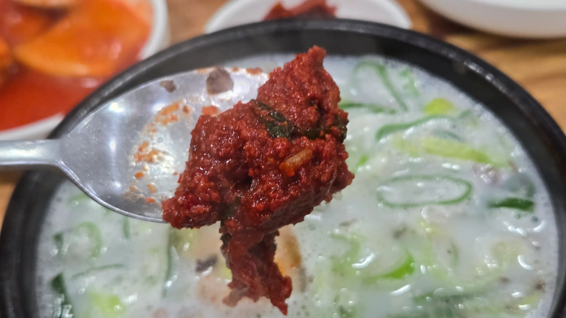 Adding a spoonful of red chilli seasoning paste to sundaegukbap turning the white pork broth into a spicy hangover soup