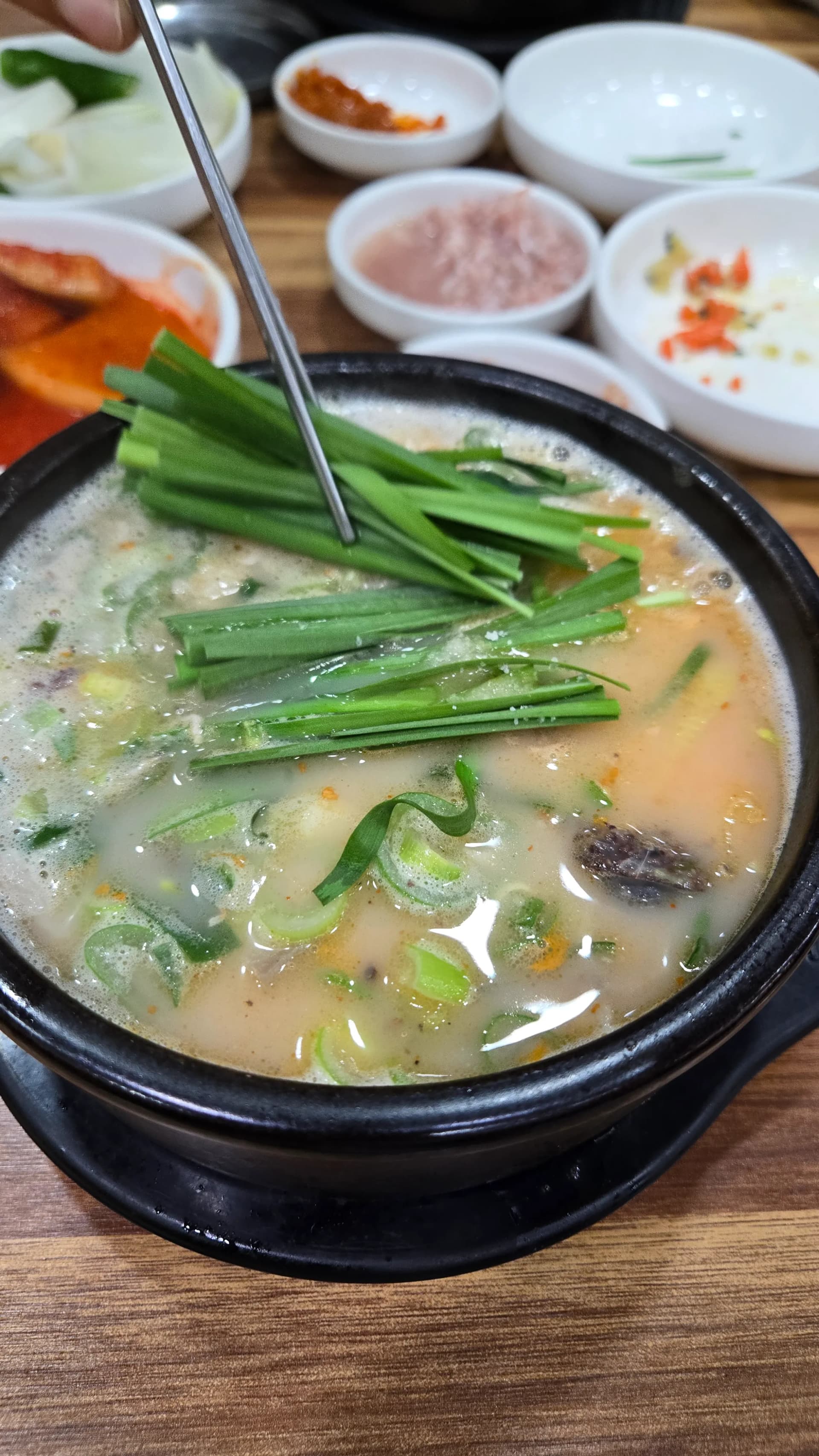 Completed sundaegukbap bowl with chives on top after seasoning with chilli paste and fermented shrimp showing the transformed broth colour