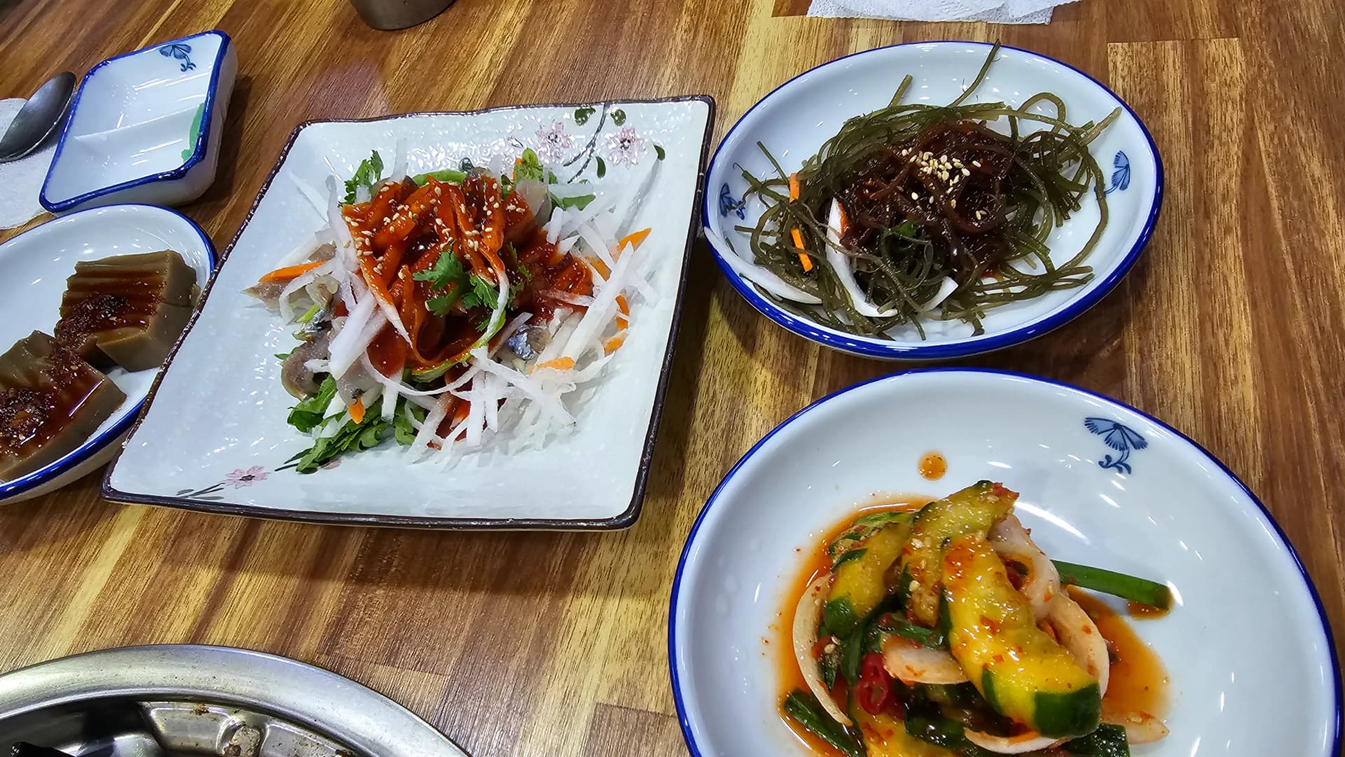 Banchan del restaurante de jogaejjim — kimchi, brotes de soja, pastelitos de arroz y dumplings servidos en la mesa