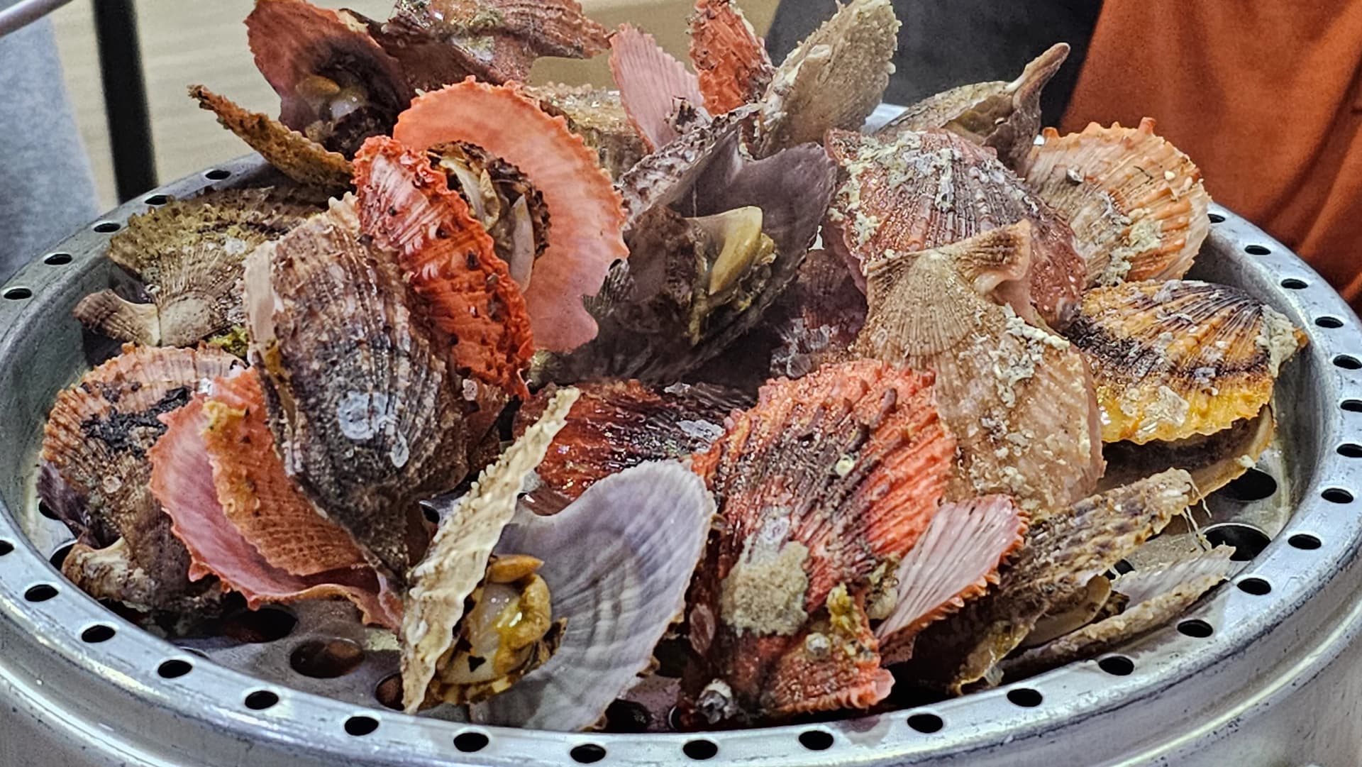 Segundo nivel de la vaporera abierto, repleto de vieiras al vapor con columnas de vapor saliendo