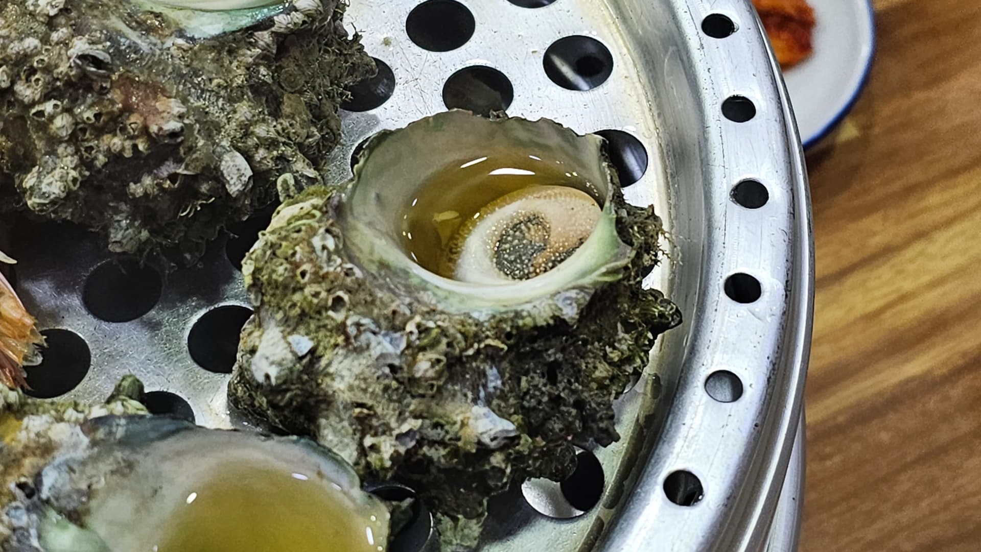 Primer plano de un caracol de mar al vapor con el jugo acumulado dentro de la concha y la carne enroscada